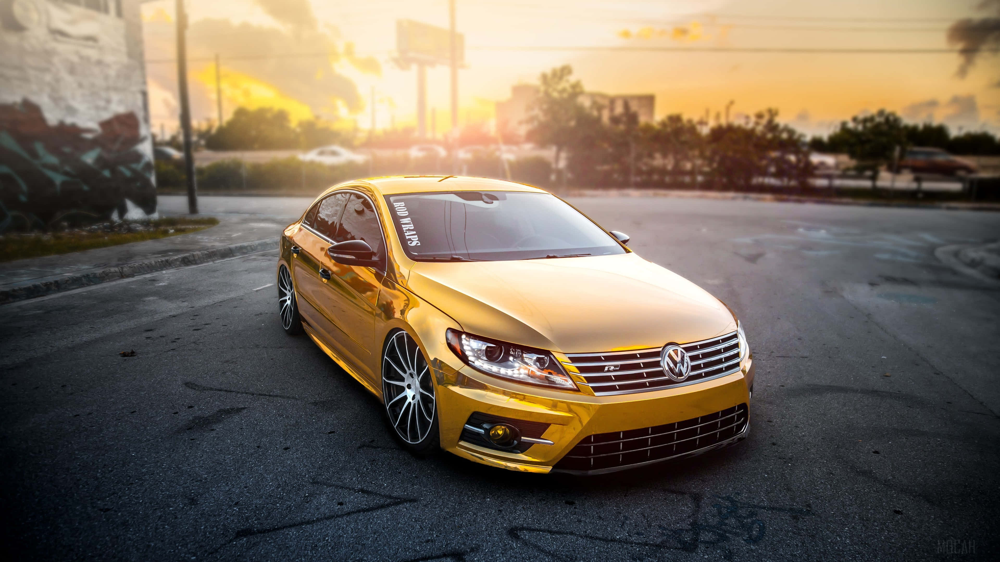 Gold Cars 桌布 壁紙 — 一輛閃閃發光的金色福斯汽車房車停在柏油路上，金色夕陽將城市街道沐浴在溫暖的色調中。