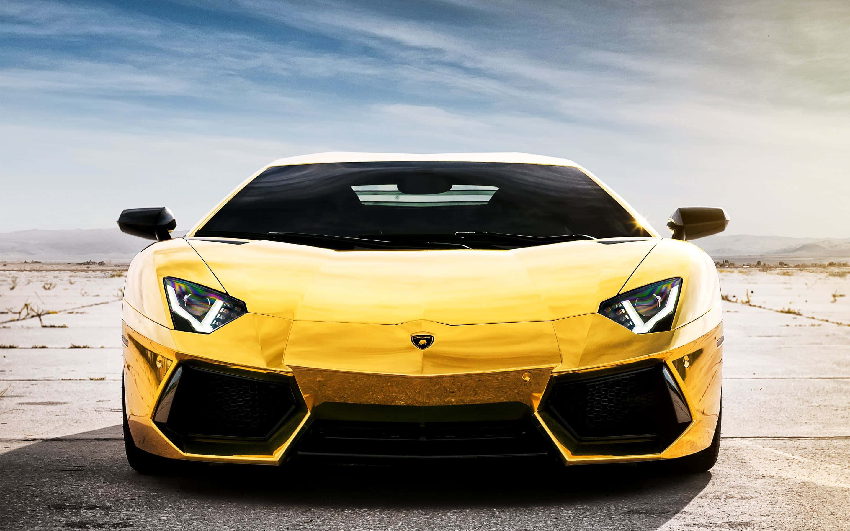 跑車 桌布 壁紙 — 一輛閃閃發光的金色藍寶堅尼 Aventador 在陽光明媚的沙漠道路上向前行駛，遠處有山脈，藍天白雲。