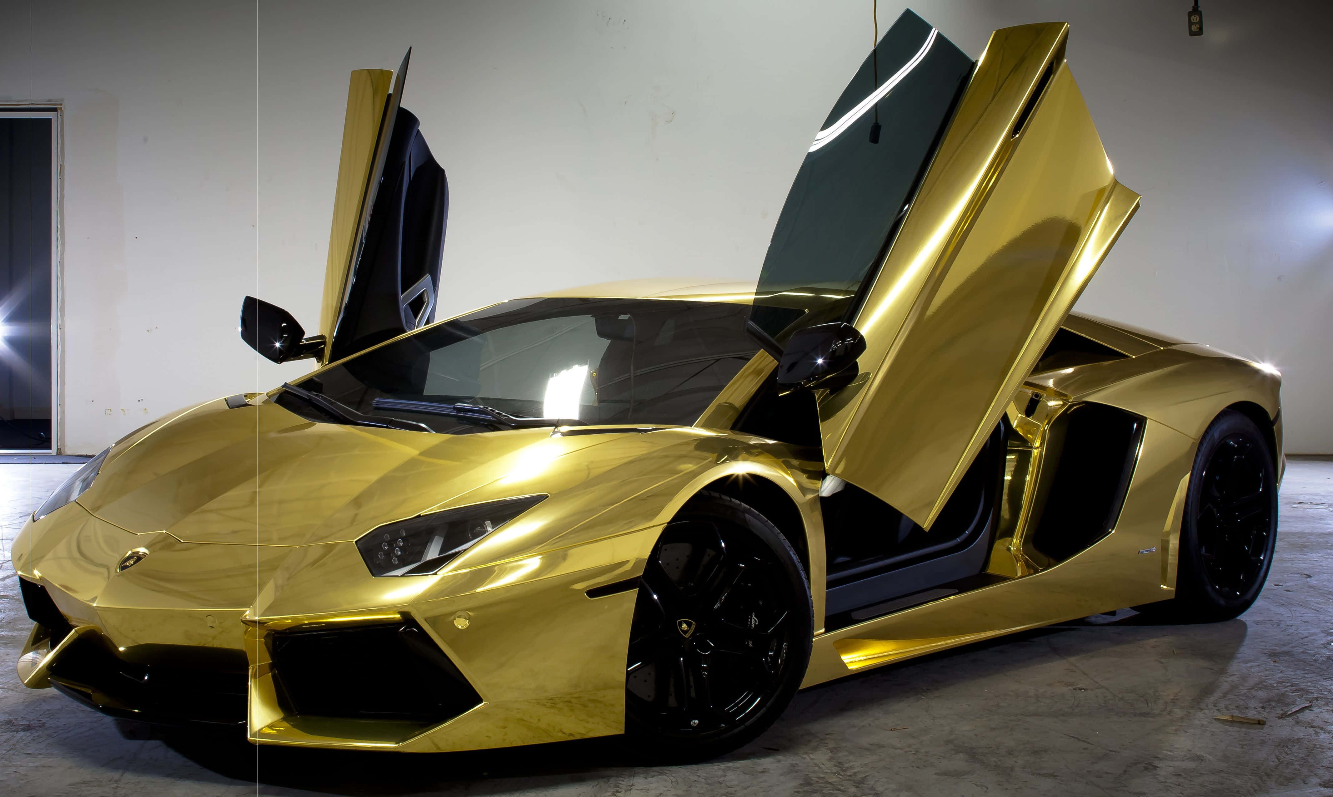 跑車 桌布 壁紙 — 一輛閃閃發光的金色藍寶堅尼 Aventador 打開鷗翼車門，在明亮的攝影棚燈光下停放在簡約的車庫中。