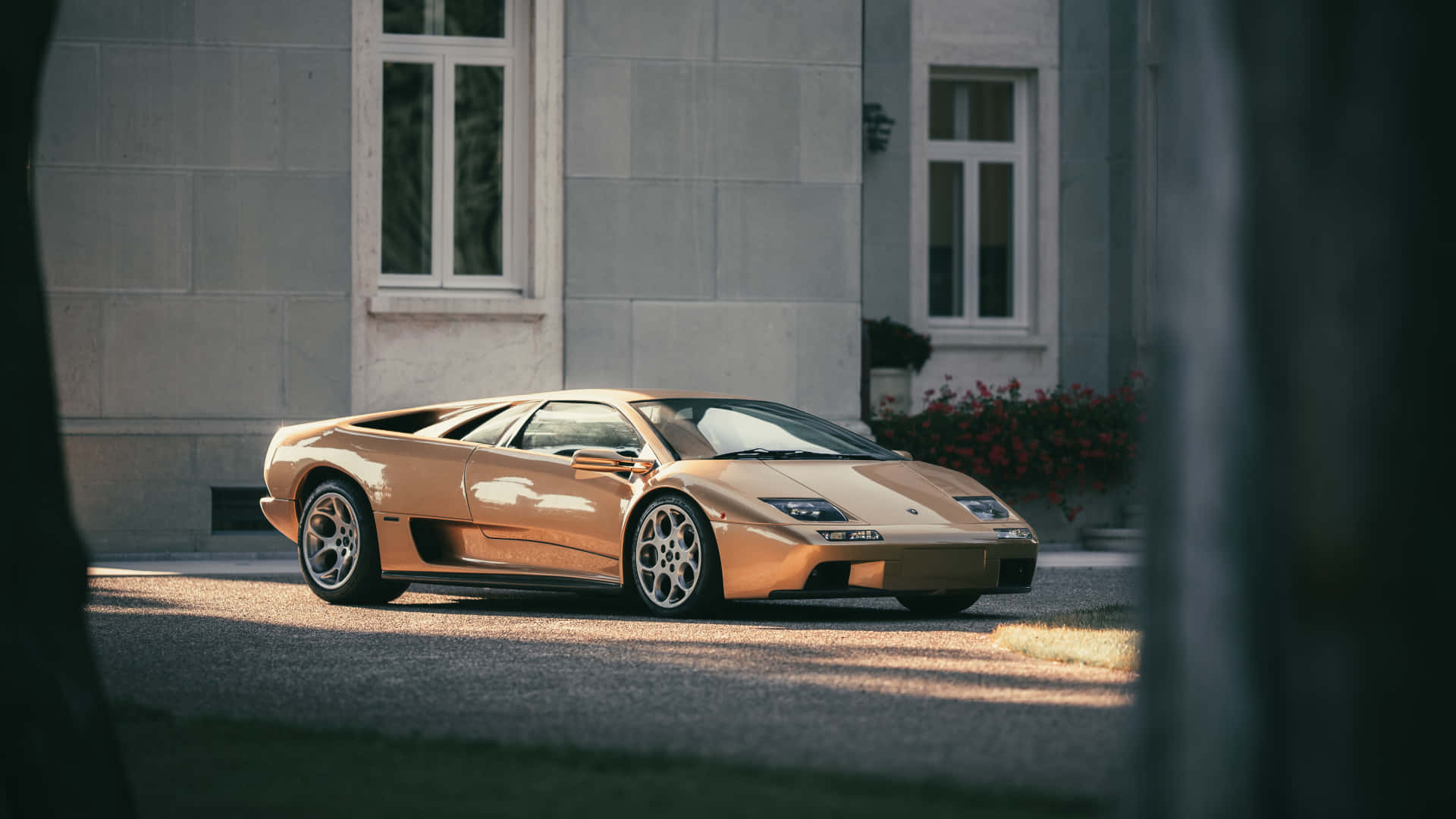 Lamborghini Diablo 桌布 壁紙 — 一輛閃閃發光的金色藍寶堅尼 Diablo 停泊在石砌豪宅前，陽光投下長長的影子。
