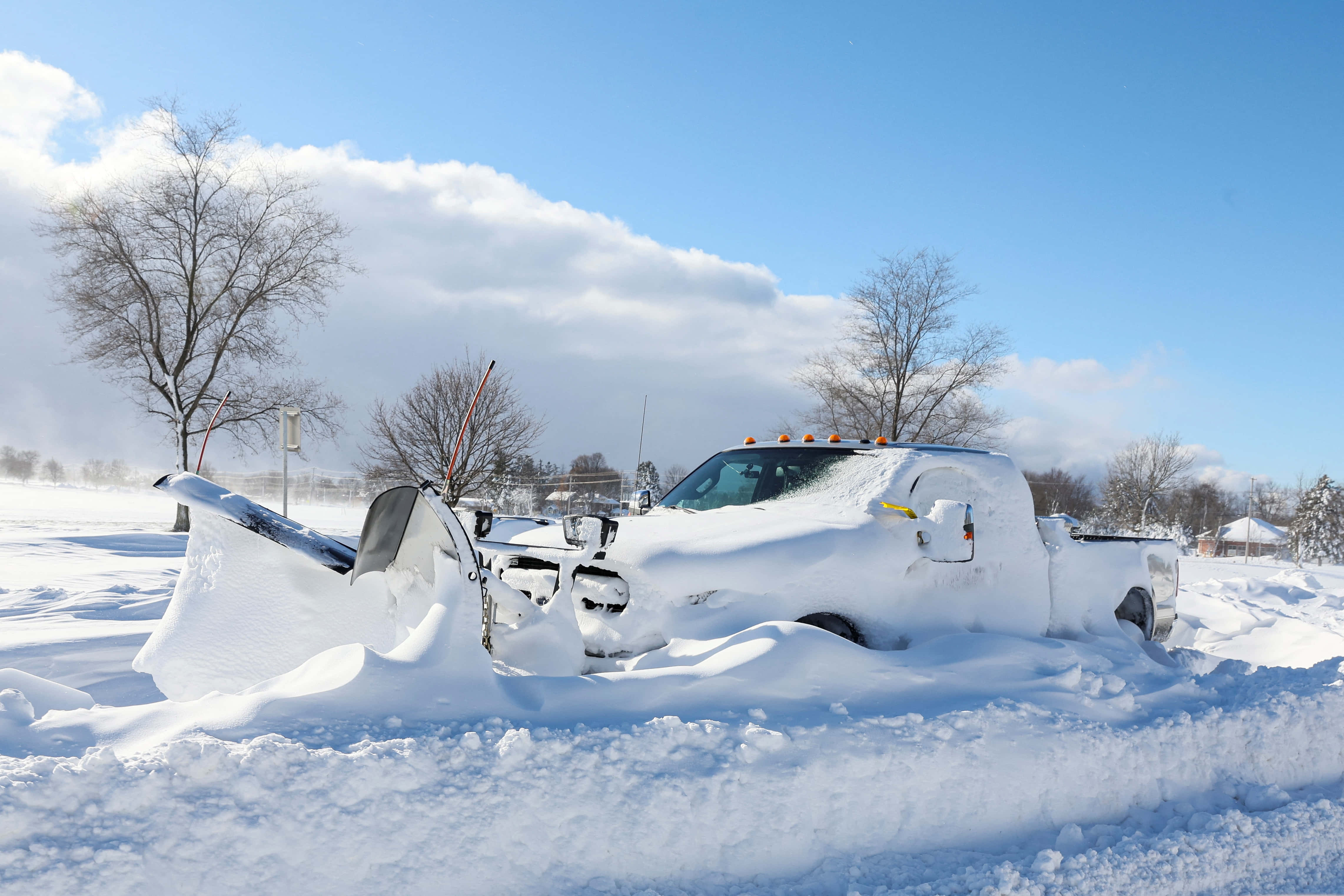 blizzard 桌布 壁紙 — 一輛除雪卡車被埋在深雪中，明亮的冬季田野上有光禿禿的樹木和藍天。