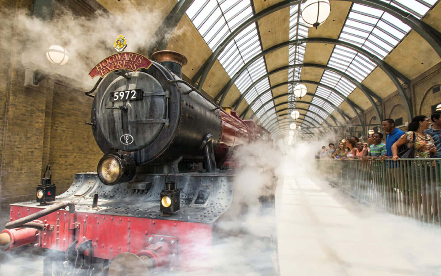 Hogwarts Express 桌布 壁紙 — 一輛雄偉的霍格華茲特快蒸汽火車在宏偉的車站噴出煙霧，興奮的訪客在欄杆後觀看。
