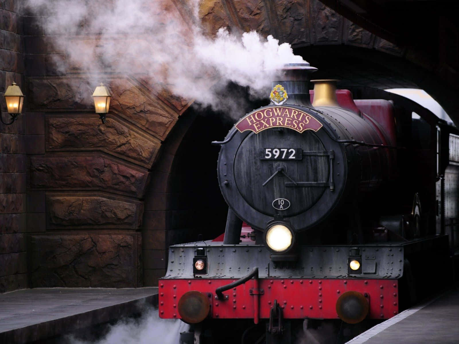 Hogwarts Express 桌布 壁紙 — 一輛雄偉的霍格華茲特快蒸汽火車從月台的石拱門中駛出，噴出白色蒸氣。