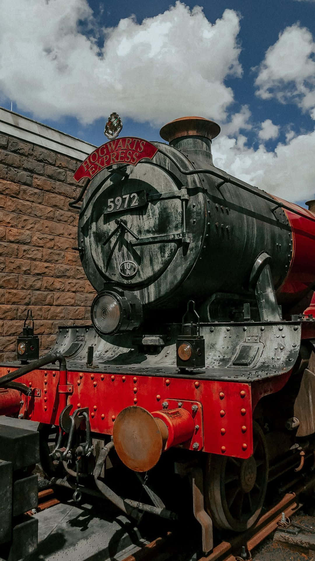 Hogwarts Express 桌布 壁紙 — 一輛雄偉的霍格華茲特快蒸汽火車頭，帶有紅色點綴和編號5972，驕傲地矗立在晴朗的藍天和蓬鬆的白雲下。