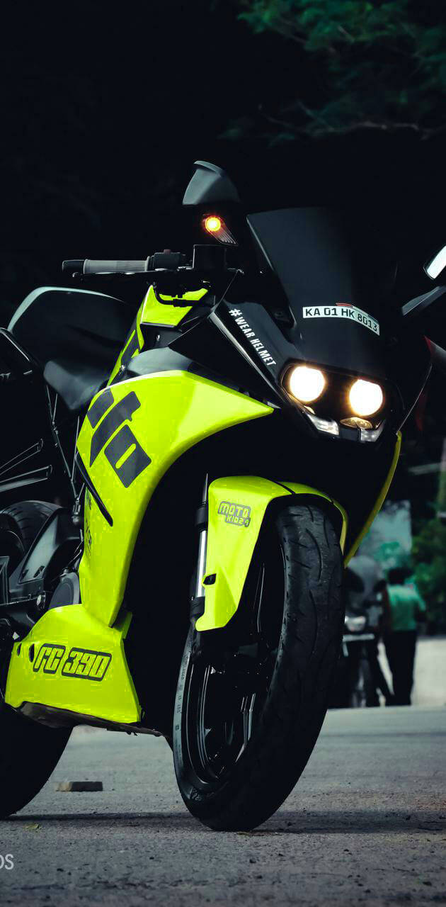 KTM RC 200 桌布 壁紙 — 一輛霓虹黃色機車，帶有發光頭燈，夜間停泊在黑暗的街道上，背景有樹木。