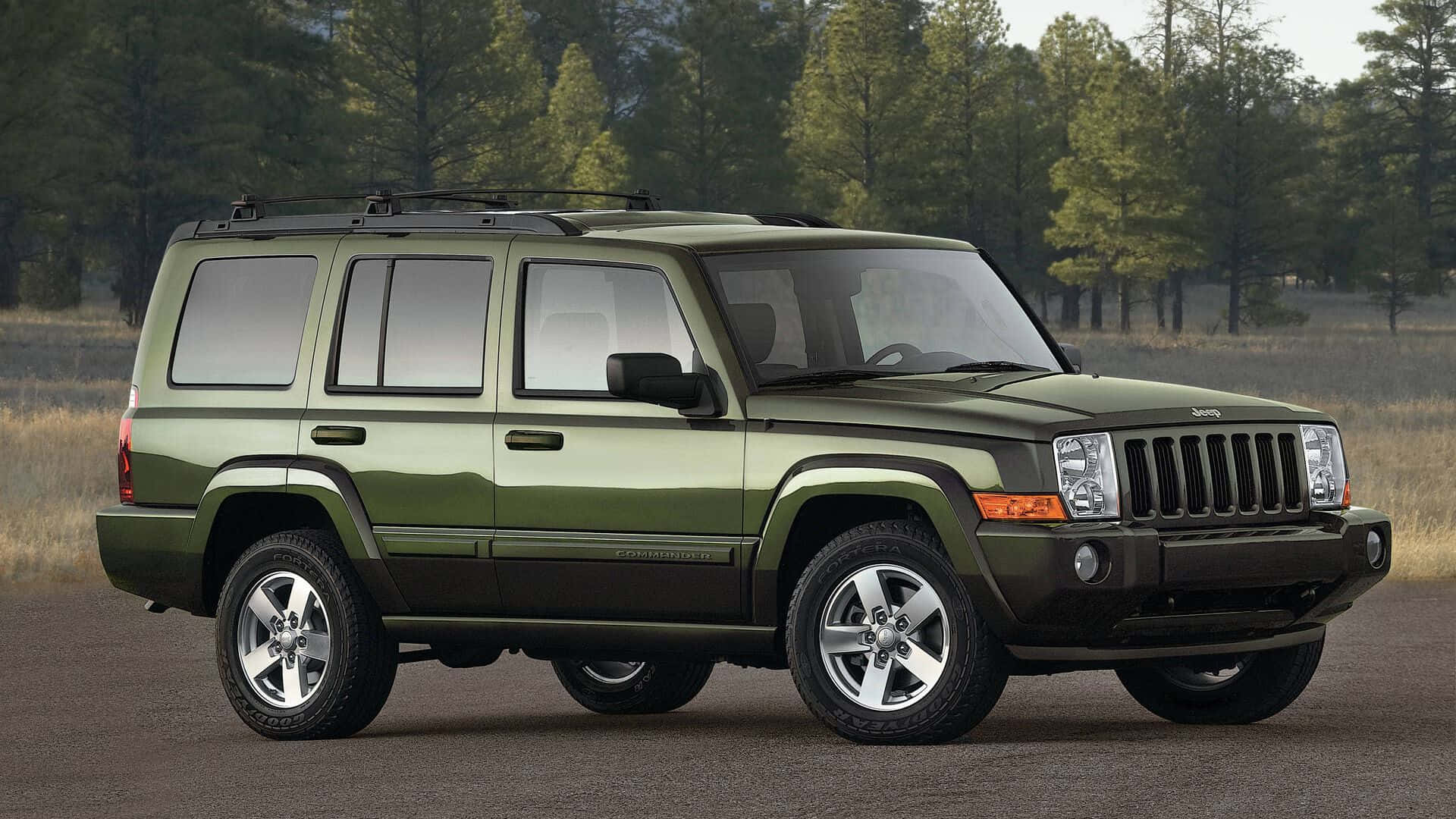 Jeep Commander 桌布 壁紙 — 一輛霧面橄欖綠色的Jeep Commander SUV停在柏油路面上，背景是森林，光線柔和。