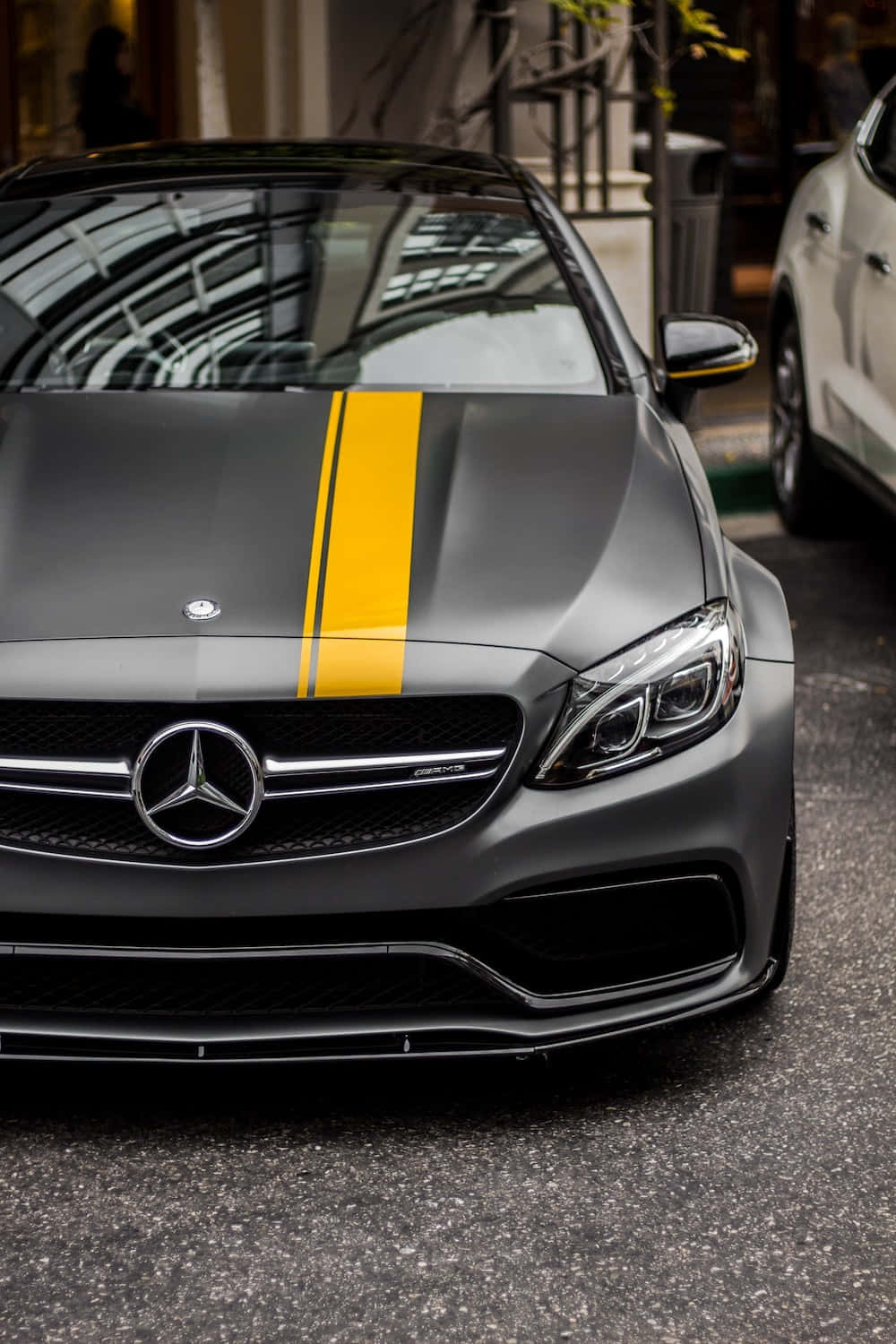 Mercedes 桌布 壁紙 — 一輛霧面灰色的梅賽德斯-AMG跑車，帶有醒目的黃色條紋，停在城市街道上。