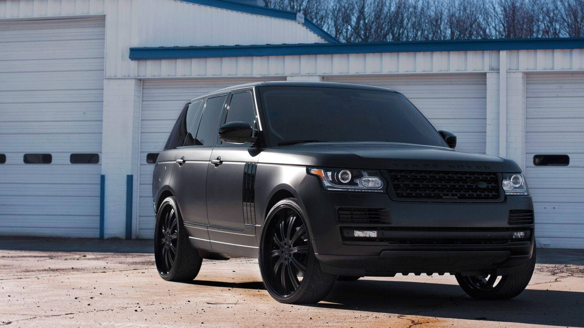 高清 桌布 壁紙 — 一輛霧面黑色Range Rover Sport配備客製黑色輪圈，在晴朗的日子停在一棟白色工業建築前。