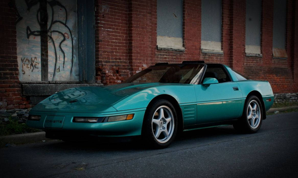 corvette 桌布 壁紙 — 一輛青綠色敞篷跑車停在一棟帶有塗鴉的風化磚砌建築前。