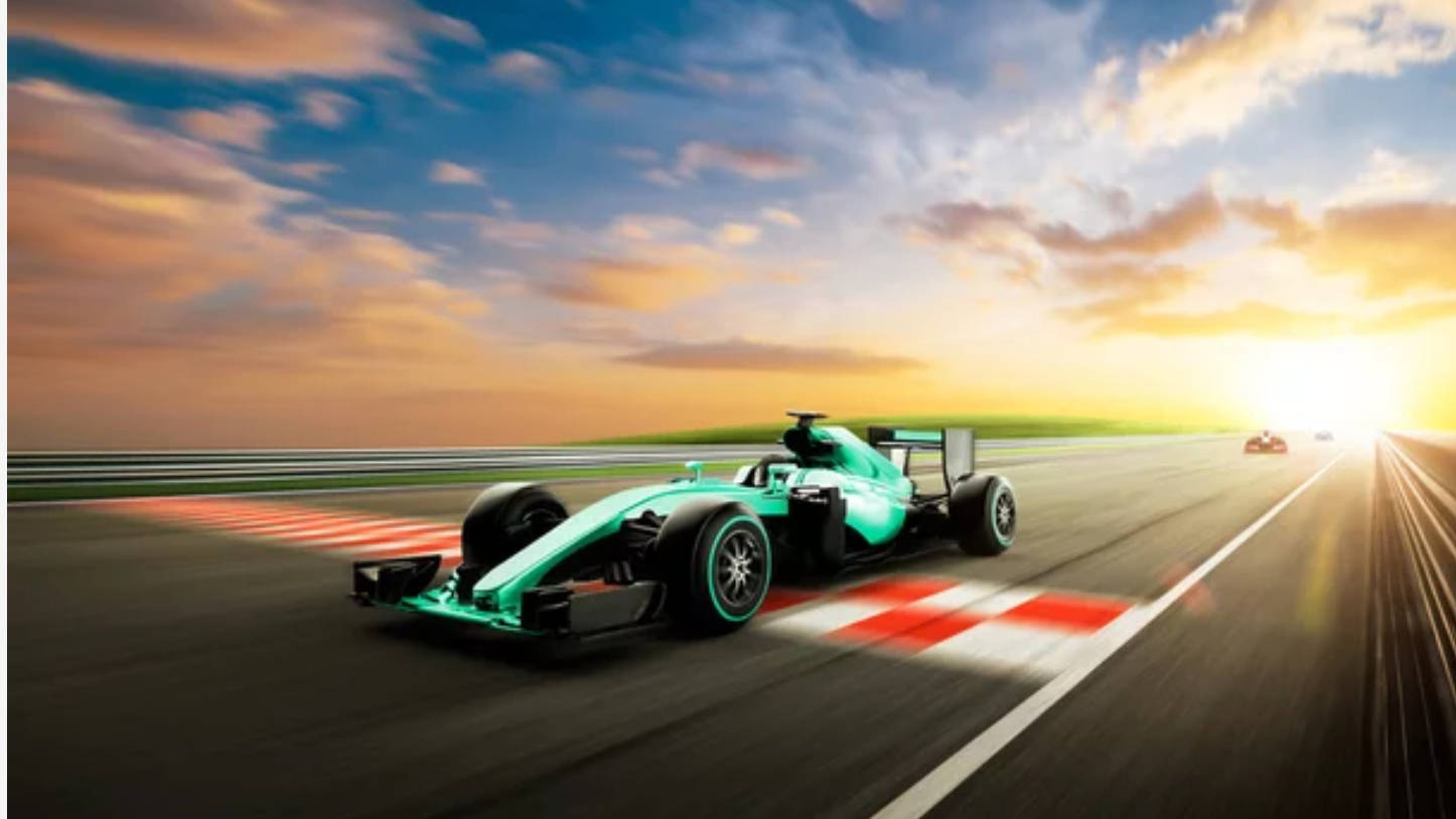 4K 桌布 壁紙 — 一輛青綠色的 Formula 1 賽車在日落時分沿著賽道疾馳，帶有動態模糊和發光的太陽光線。