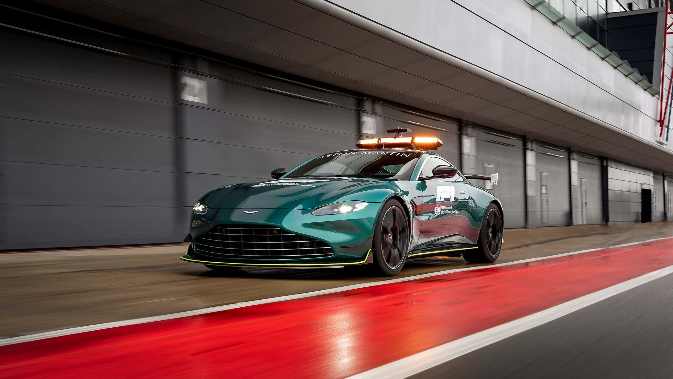 奧斯頓馬丁 桌布 壁紙 — 一輛青綠色的Aston Martin賽車在紅色線的賽道上飛馳，帶有動態模糊和發光的橙色燈光。