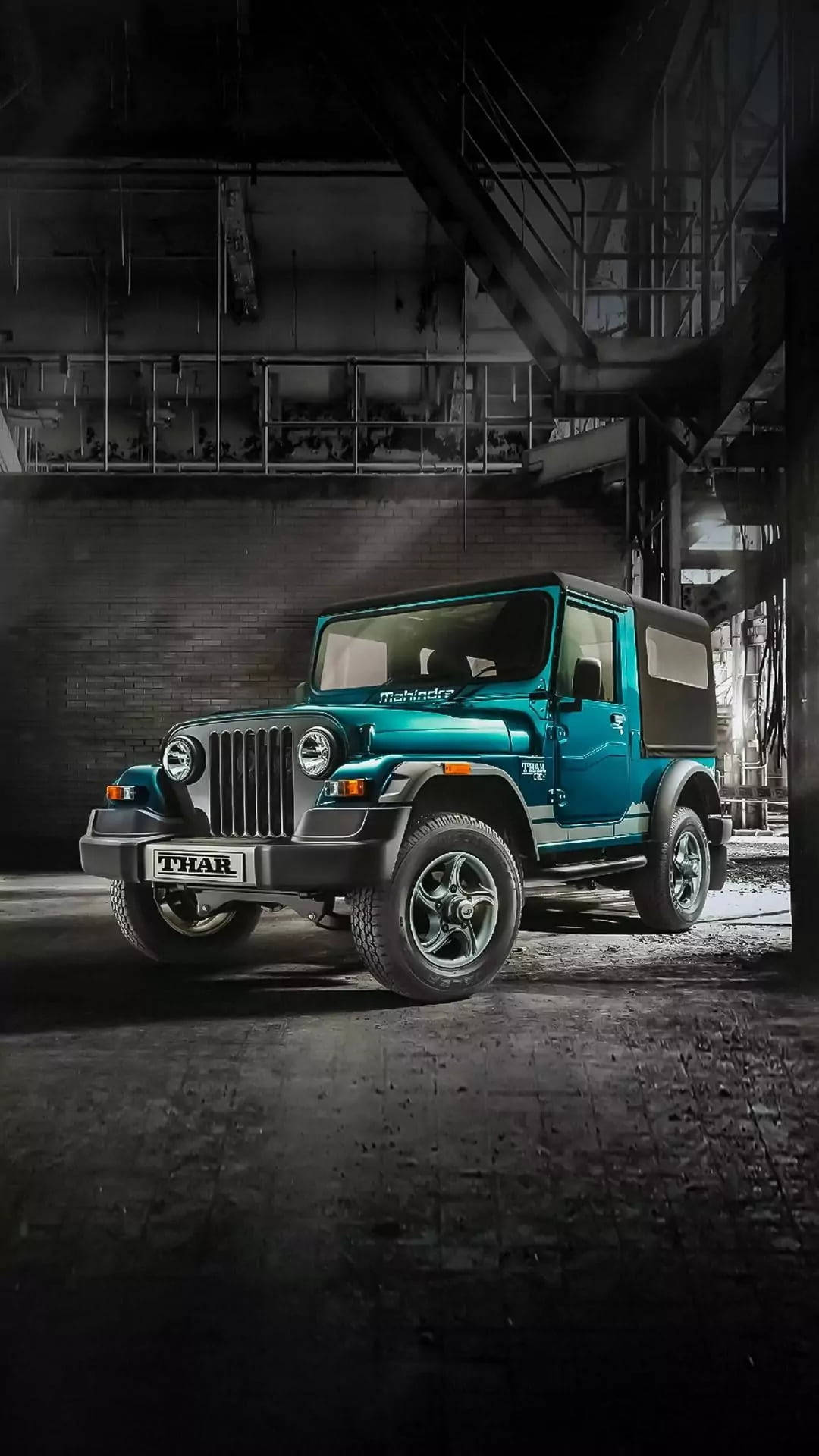 手機 桌布 壁紙 — 一輛青綠色的Mahindra Thar SUV在一個粗糙的工業倉庫中戲劇性地照亮，露出橫樑和磚牆。