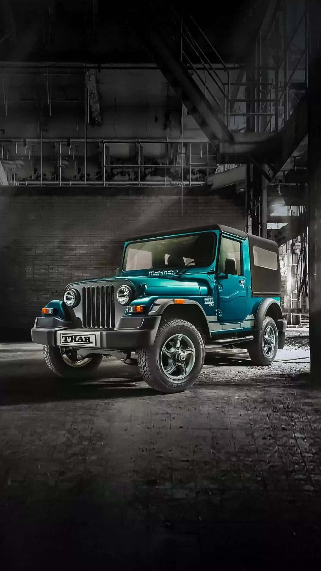 吉普 桌布 壁紙 — 一輛青綠色的Mahindra Thar SUV在燈光昏暗的工業倉庫中，在戲劇性的聚光燈下傲然矗立。