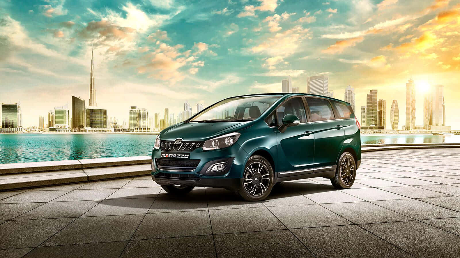 Mahindra 桌布 壁紙 — 一輛青綠色的Marazzo小型貨車停泊在瓷磚鋪設的海濱長廊上，背景是杜拜天際線和哈里發塔，沐浴在金色的日落光芒中。