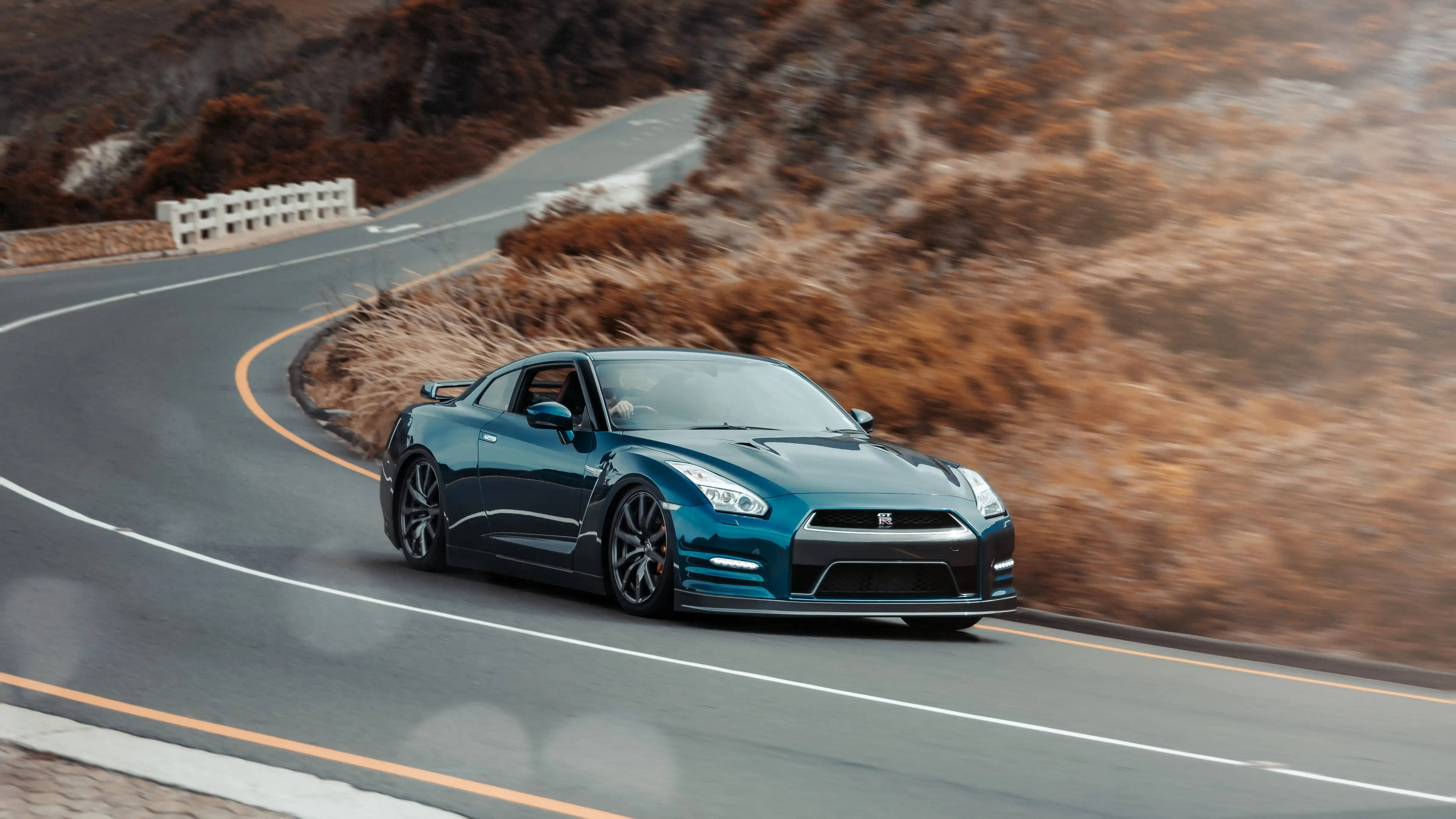 Nissan 桌布 壁紙 — 一輛青綠色的日產GT-R在蜿蜒的山路上疾馳，背景是模糊的秋日山丘。