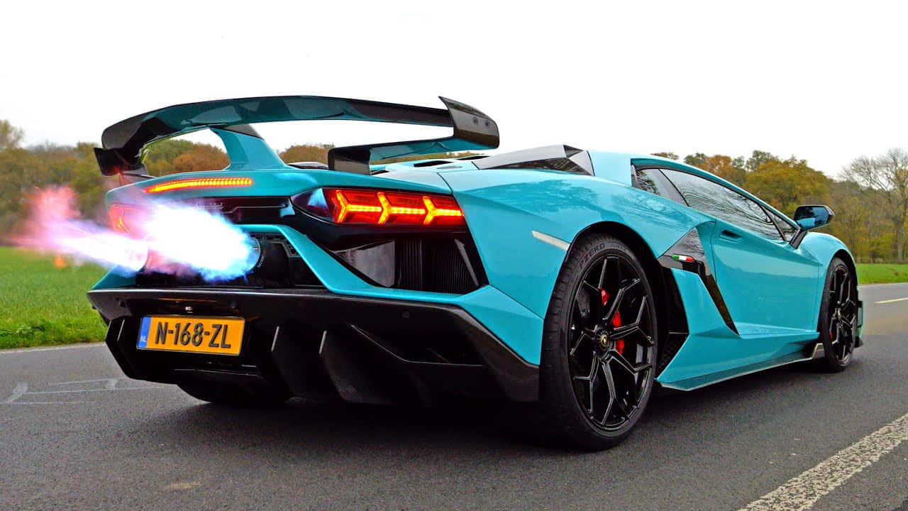 Lamborghini On Fire 桌布 壁紙 — 一輛青綠色的藍寶堅尼 Aventador SVJ 在鄉間道路上呼嘯而過，後方的噴射引擎噴出藍色火焰。