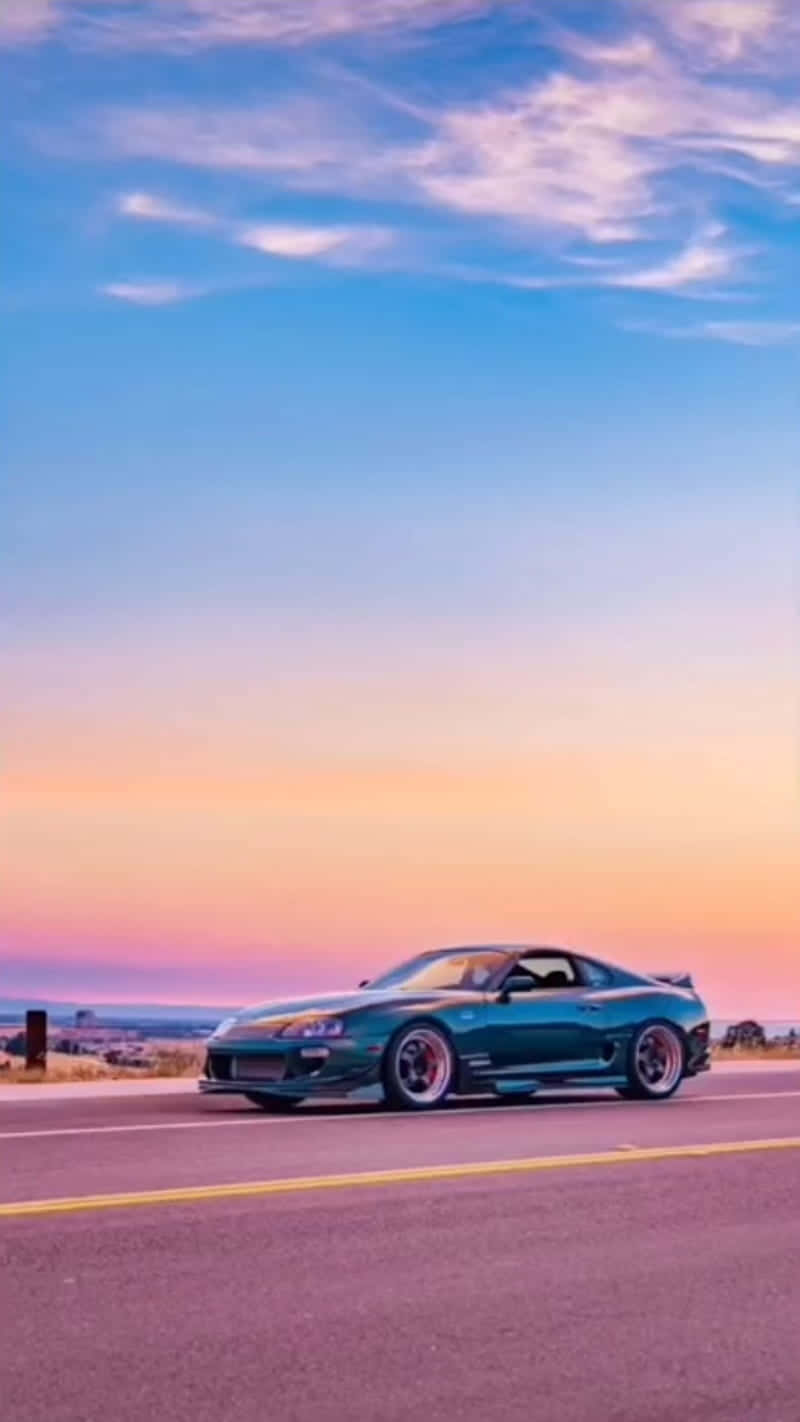Blue Car 桌布 壁紙 — 一輛青綠色跑車在沙漠公路上行駛，天空呈現粉紅、橙和藍色的鮮豔暮色。