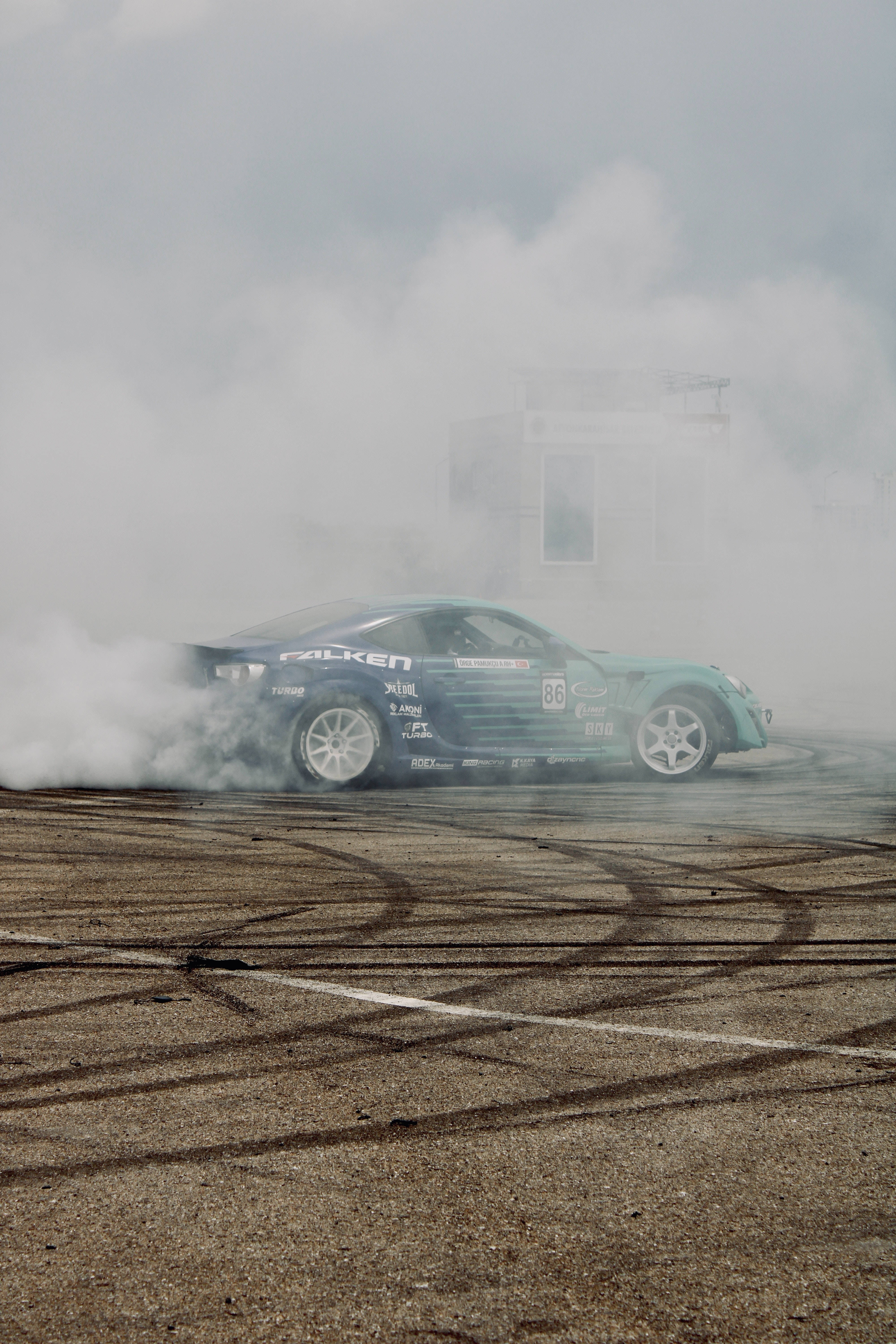 drifting 桌布 壁紙 — 一輛青綠色飄移車在陰天的塵土賽道上劃出緊密圓圈，冒出濃煙。