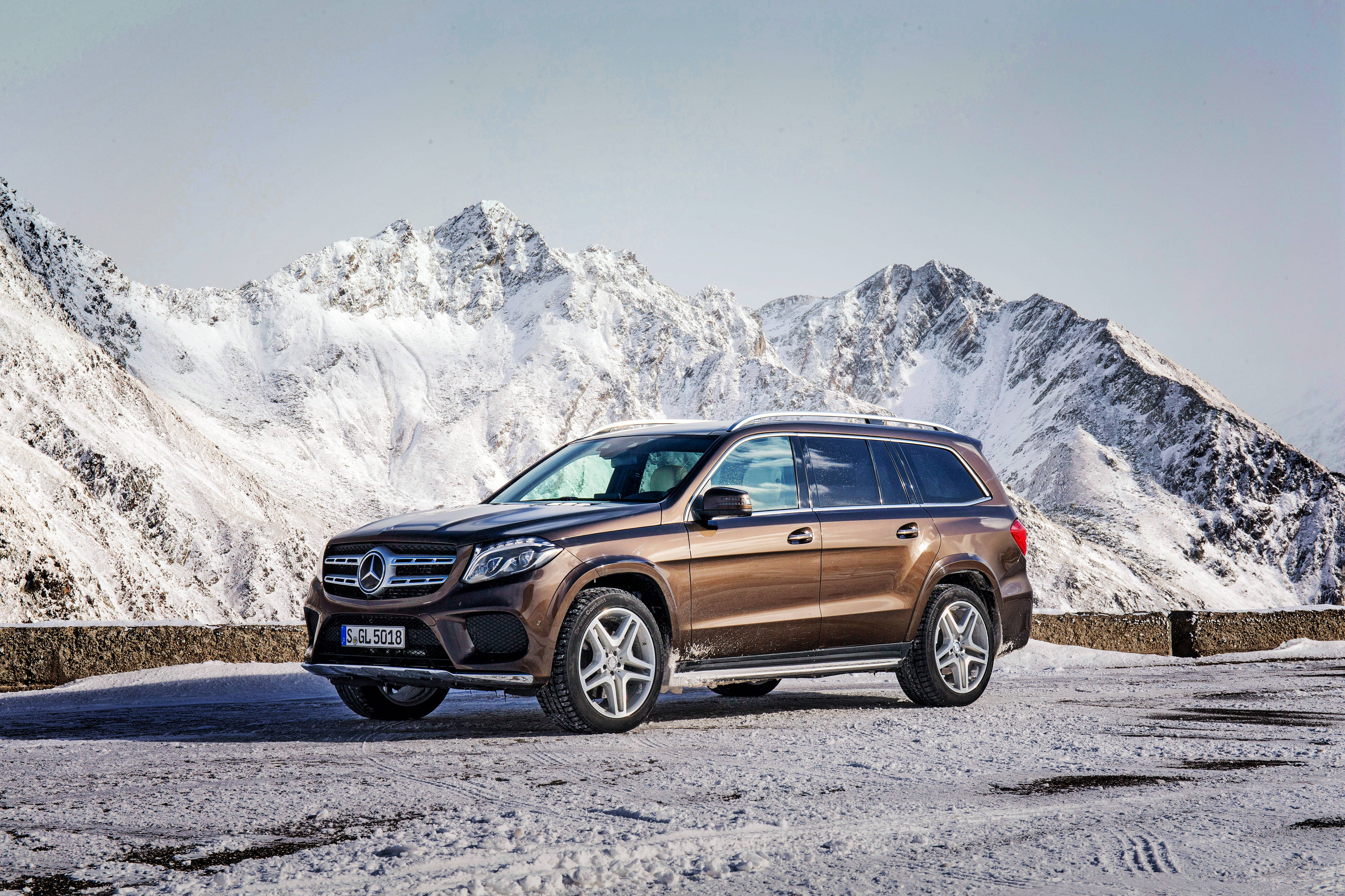 跑車 桌布 壁紙 — 一輛青銅色 Mercedes GLS SUV 停泊在積雪的路邊，背後是晴朗天空下雄偉的雪山。