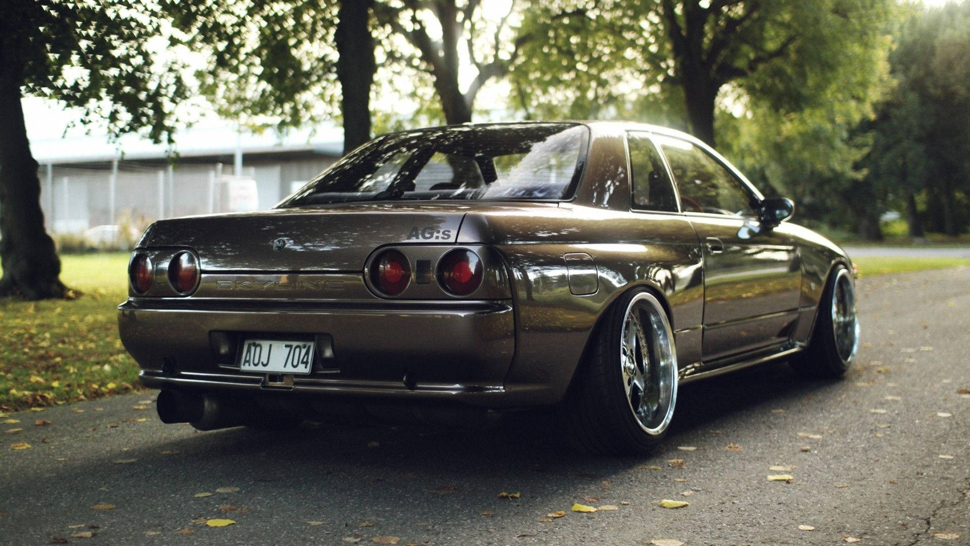 一輛青銅色日產Skyline R32配備定制輪圈，在日落時分停泊在綠樹成蔭的道路上。 — 4K Jdm 壁紙