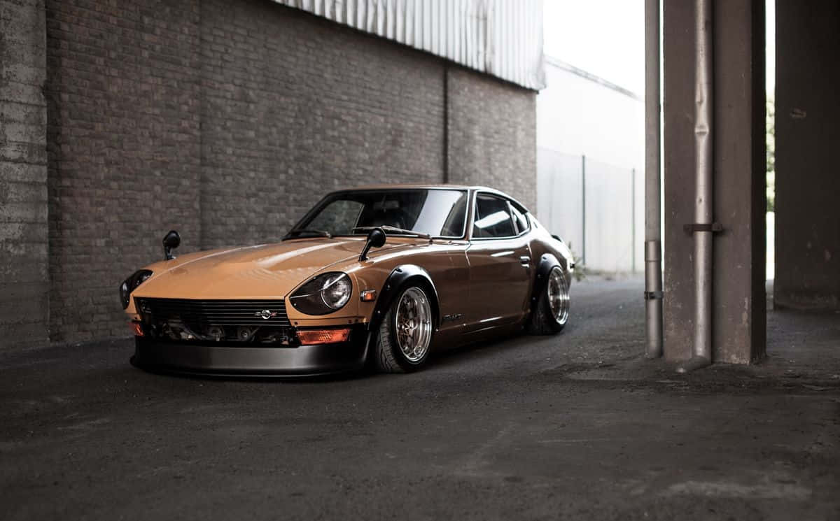 Datsun 桌布 壁紙 — 一輛青銅色經典跑車配備訂製輪圈，在漫射光下低伏於粗糙的工業倉庫中。