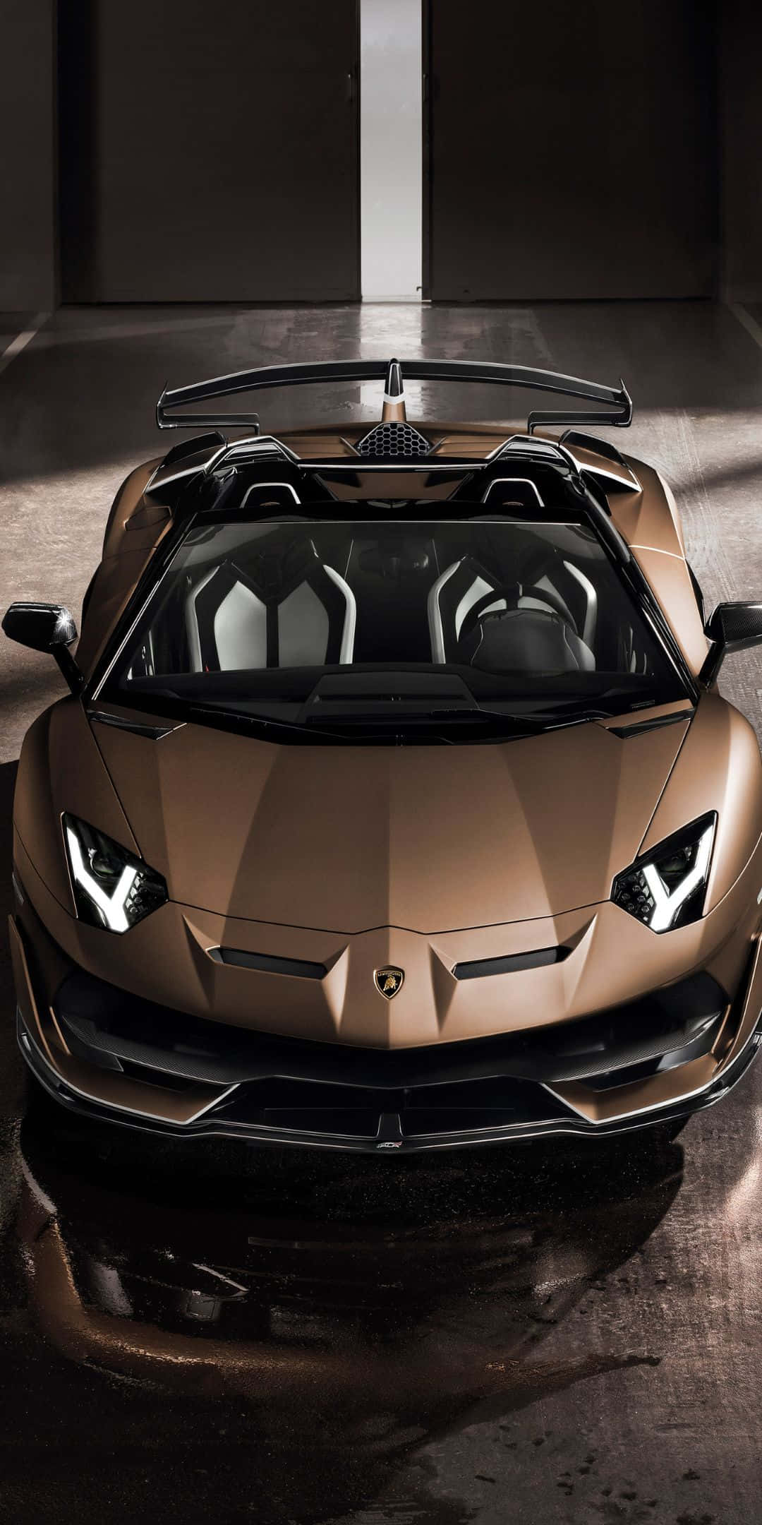 Pixel 3 Lamborghini 桌布 壁紙 — 一輛青銅色藍寶堅尼 Aventador Roadster 在簡約時尚、帶有反光濕地板的車庫中，於戲劇性燈光下閃閃發光。