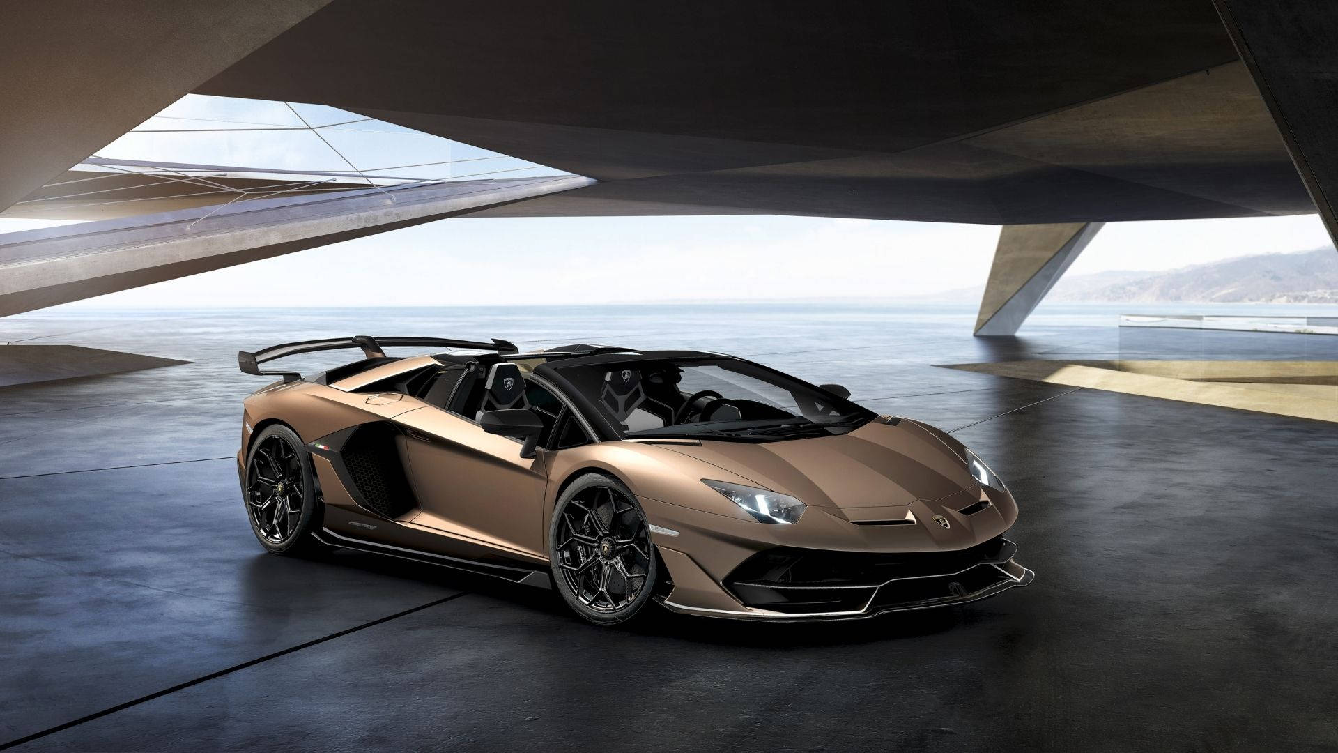 蘭博基尼 桌布 壁紙 — 一輛青銅色藍寶堅尼Aventador SVJ Roadster在自然光下，於一座俯瞰海洋的現代混凝土建築內閃閃發光。