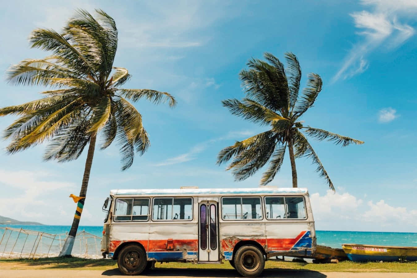 Jamaica 桌布 壁紙 — 一輛風化的彩色巴士停泊在棕櫚樹旁，背景是明亮的藍天和碧綠色的海洋。