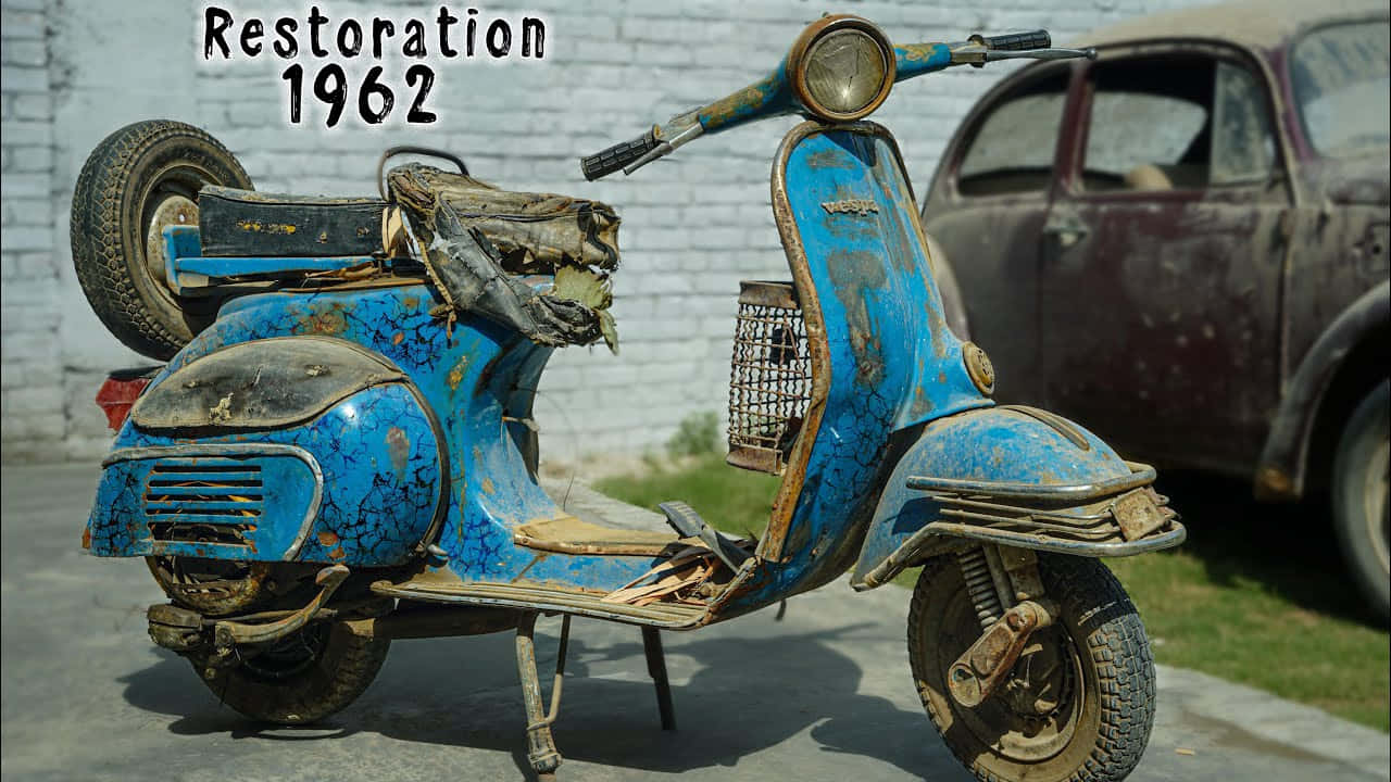 scooter 桌布 壁紙 — 一輛風化的藍色1962年Vespa摩托車，油漆龜裂生鏽，停在一輛褪色的汽車旁邊，背景是白色磚牆。