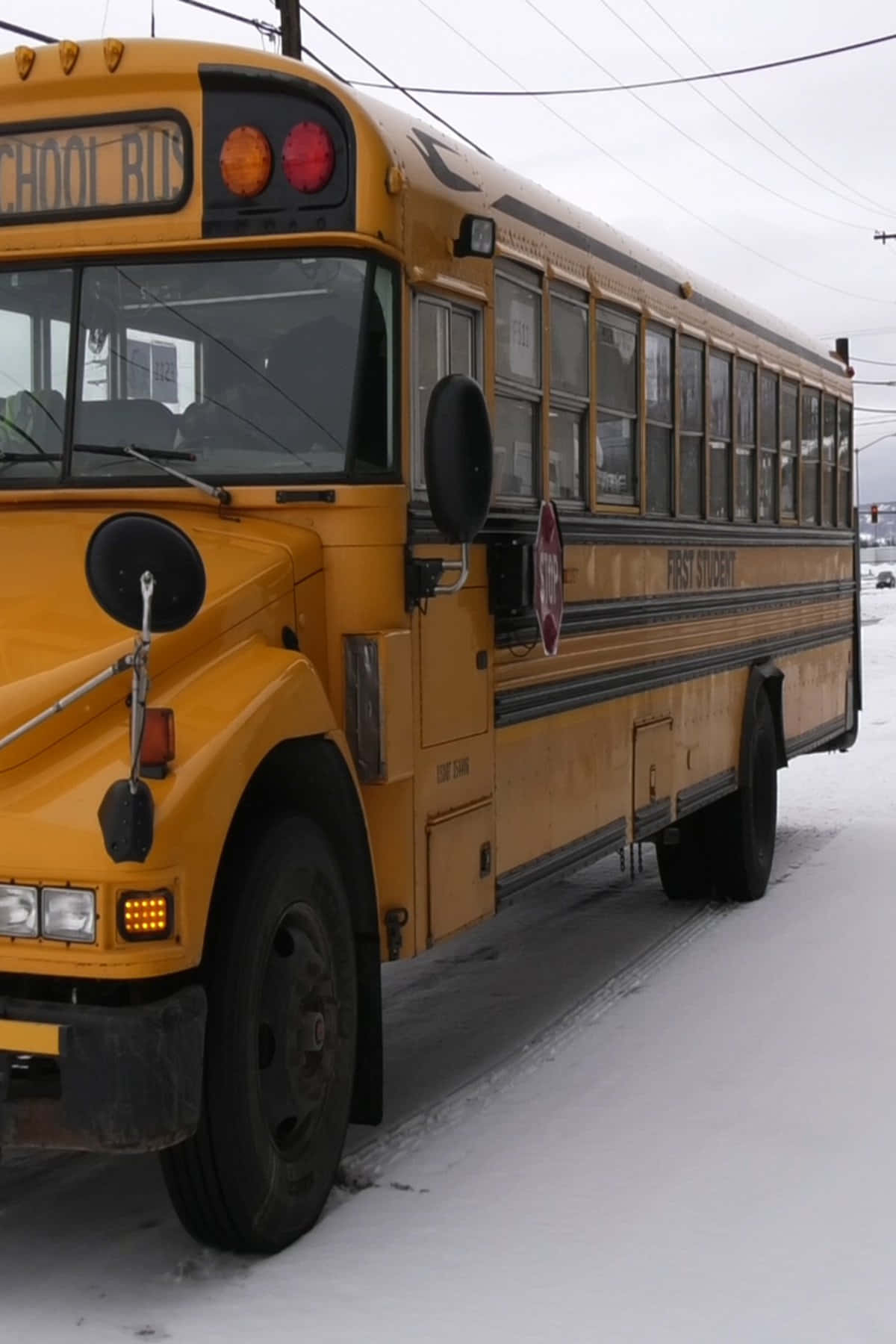 Yellow School Bus 桌布 壁紙 — 一輛風化的黃色校車停放在積雪的停車場，天空陰沉，頭頂有電線。