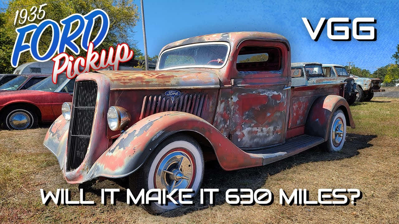 Ford Truck 桌布 壁紙 — 一輛飽經風霜的1935年福特皮卡，紅色油漆剝落，帶有鍍鉻裝飾，停在乾燥的草地上，背景是清澈的藍天。