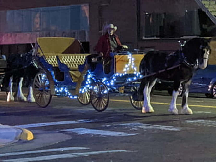 Cowboy Christmas 桌布 壁紙 — 一輛飾有藍色燈光的馬車在夜間滑過白雪覆蓋的城市街道。