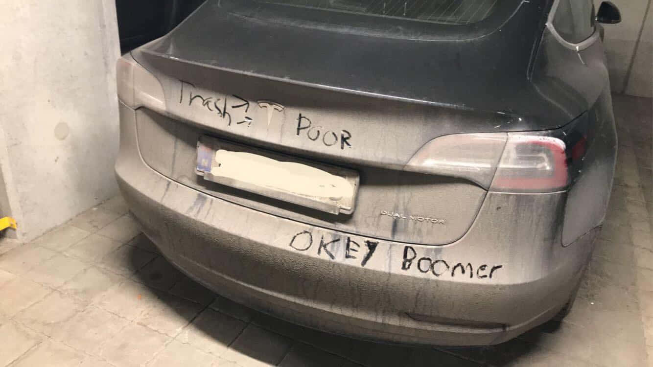 Dirty 桌布 壁紙 — 一輛骯髒的灰色Tesla，在混凝土車庫中後保險桿上噴有'Trash Poor'和'Okey Boomer'字樣。