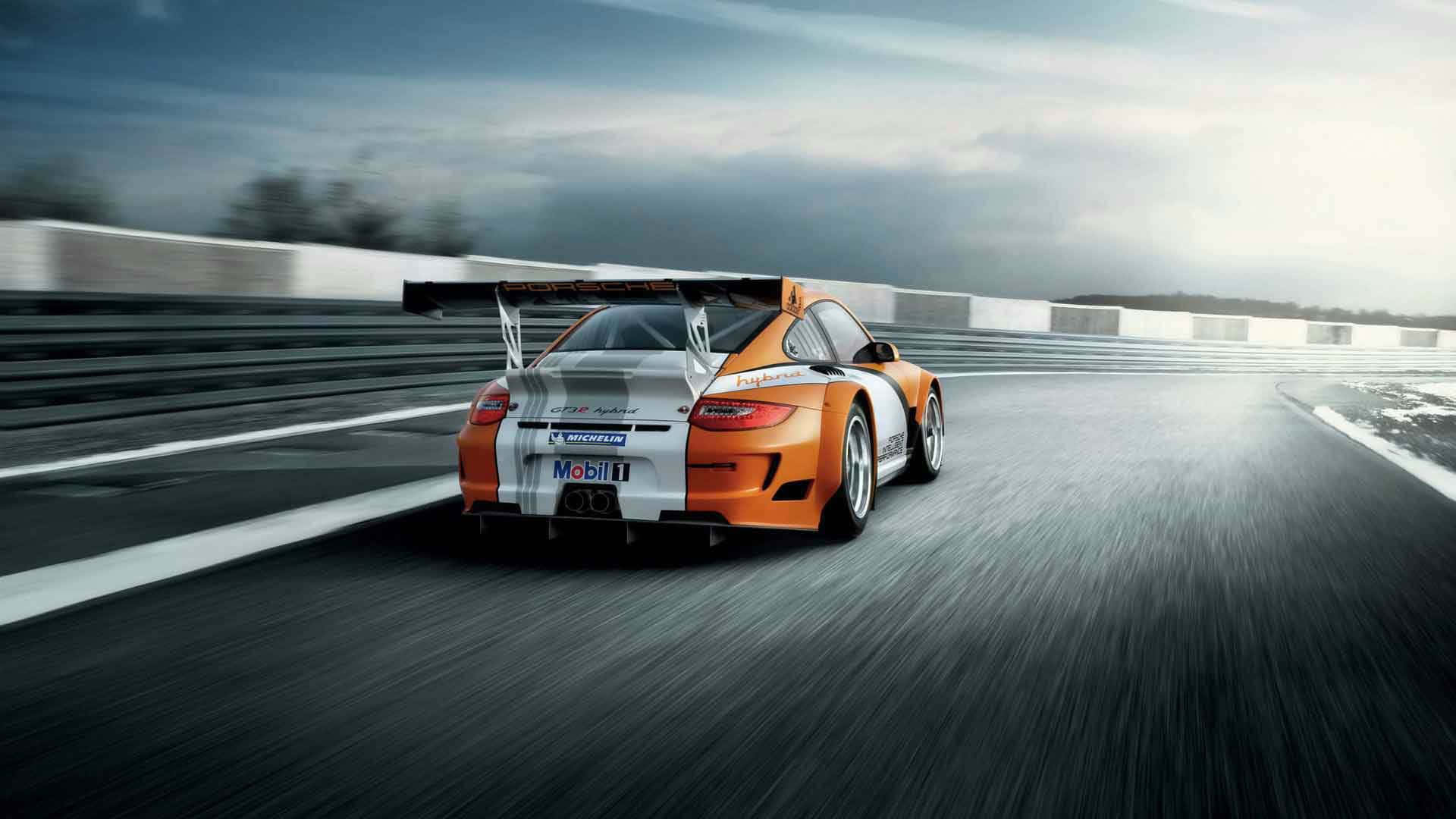 Racing Games 桌布 壁紙 — 一輛高速的橙色和白色保時捷賽車，帶有大型後翼，在陰天潮濕的賽道上飛馳。