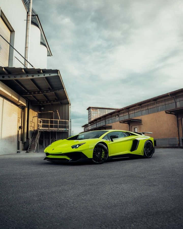 race car 桌布 壁紙 — 一輛鮮亮的萊姆綠色藍寶堅尼 Aventador SVJ 停放在工業庭院中，天空多雲。