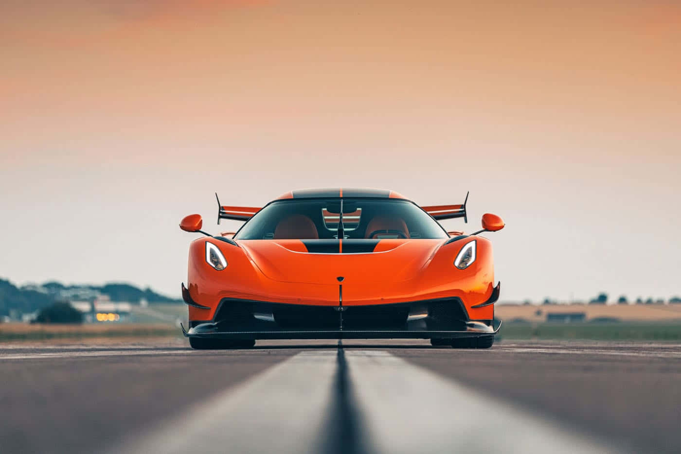 Koenigsegg 桌布 壁紙 — 一輛鮮橙色Koenigsegg超跑在日落時分面向跑道，天空溫暖發光。