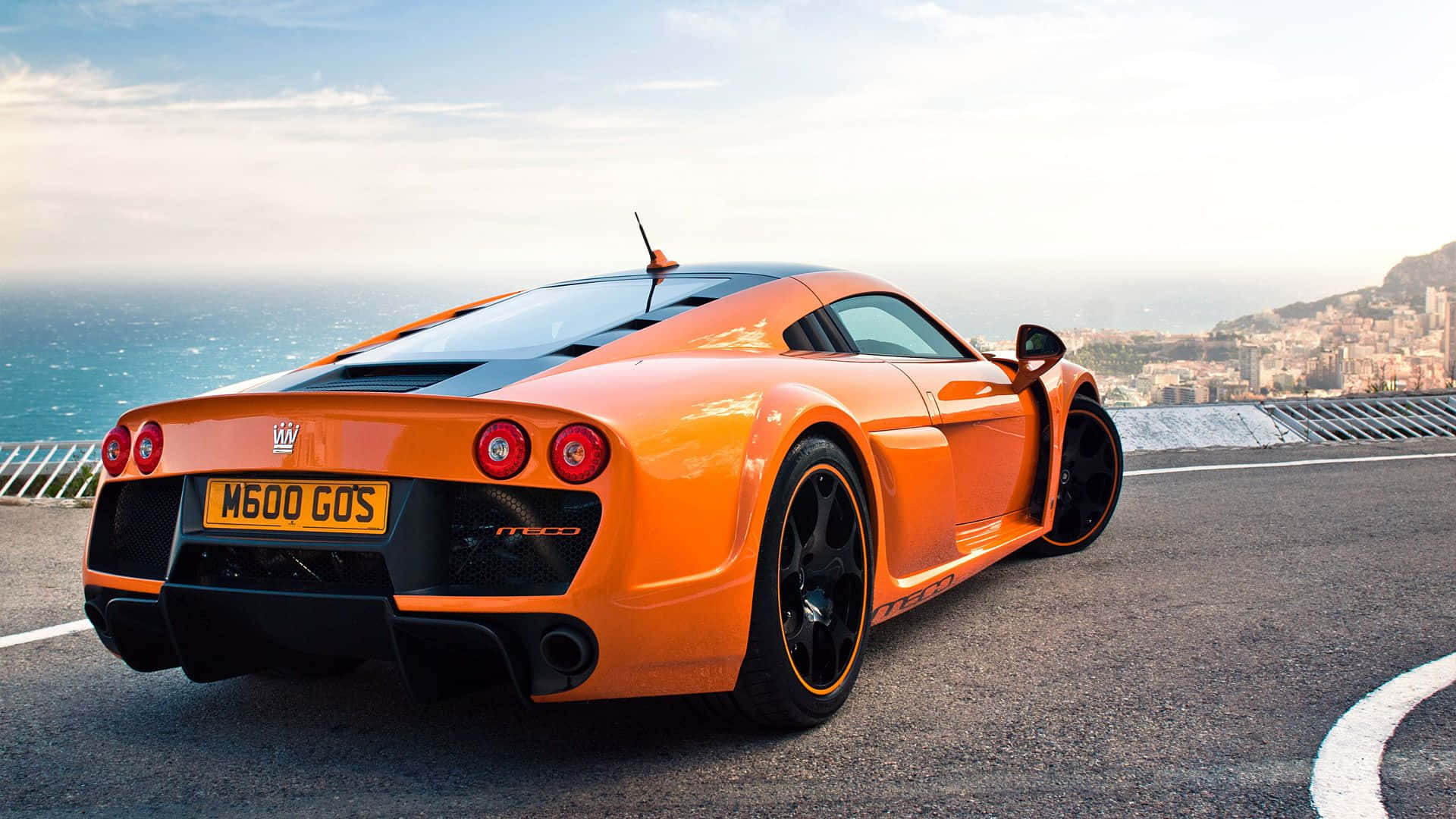 跑車 桌布 壁紙 — 一輛鮮橙色McLaren F1超級跑車停泊在俯瞰地中海的沿海道路上，遠處有城市景觀。