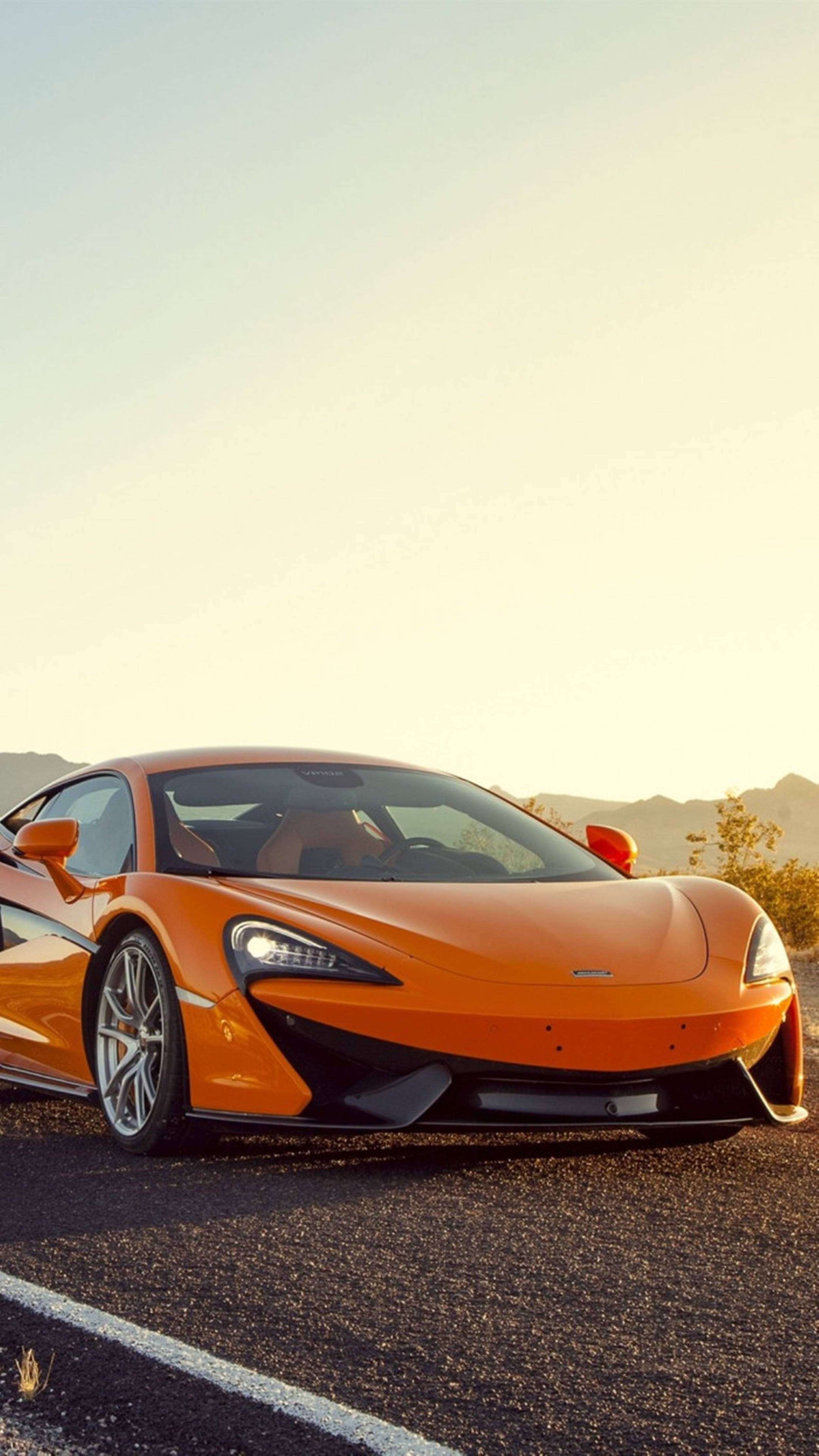 Luxury 桌布 壁紙 — 一輛鮮橙色McLaren跑車停在柏油路上，背景是山脈和金色夕陽天空。