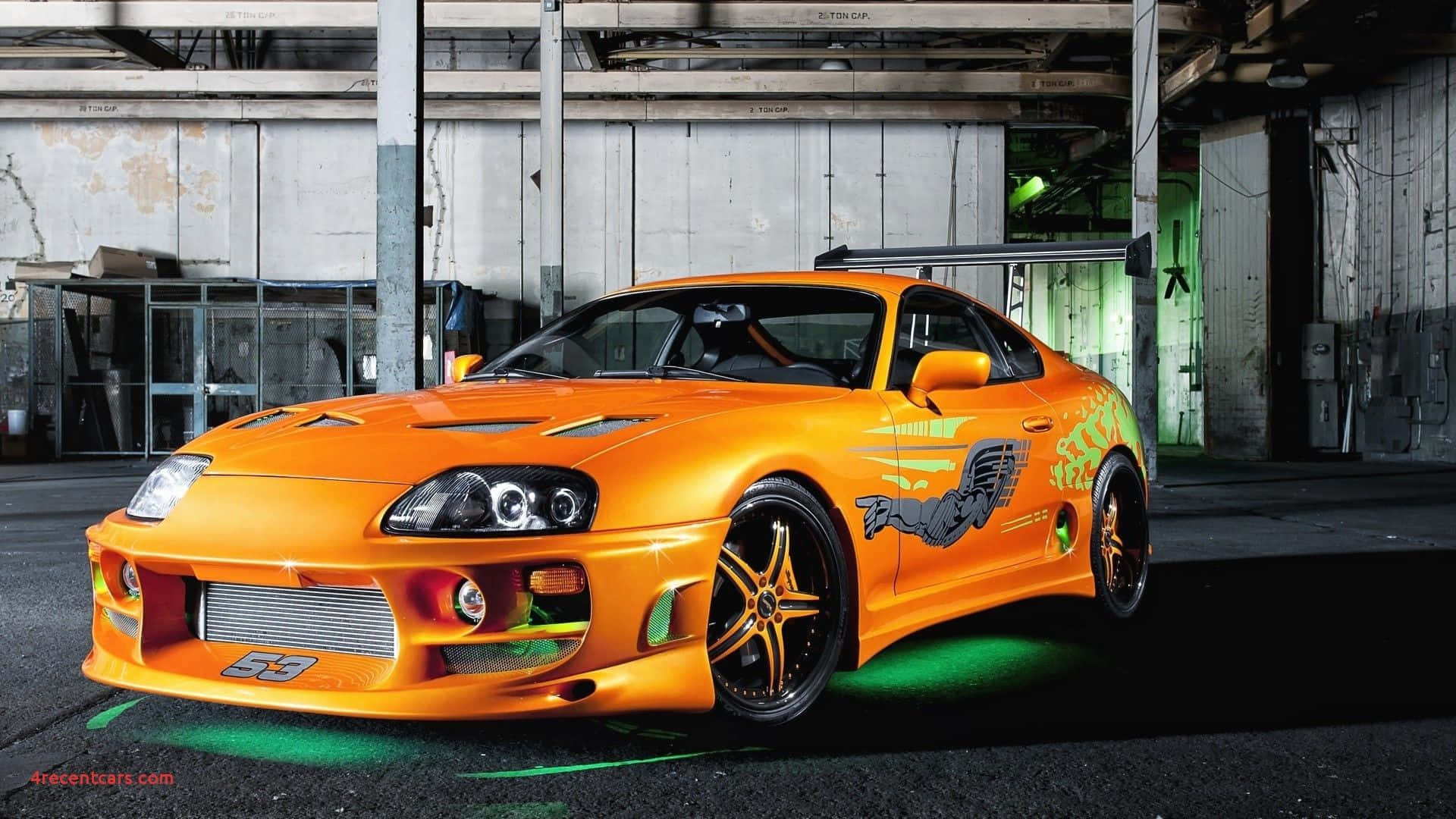 Fast And Furious 1 桌布 壁紙 — 一輛鮮橙色改裝豐田Supra，帶綠色底盤燈，停放在粗糙的工業倉庫中。