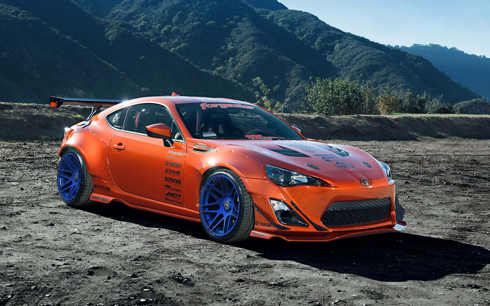 橙色改裝跑車，藍色輪圈，停泊在山邊泥濘賽道。 — Toyota Supra Mk4 壁紙