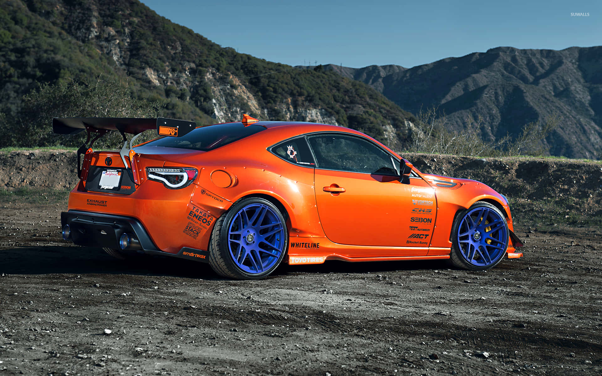 橙色訂製跑車配藍色輪胎，停泊在山附近的泥濘賽道上 — Toyota Supra Mk4 壁紙