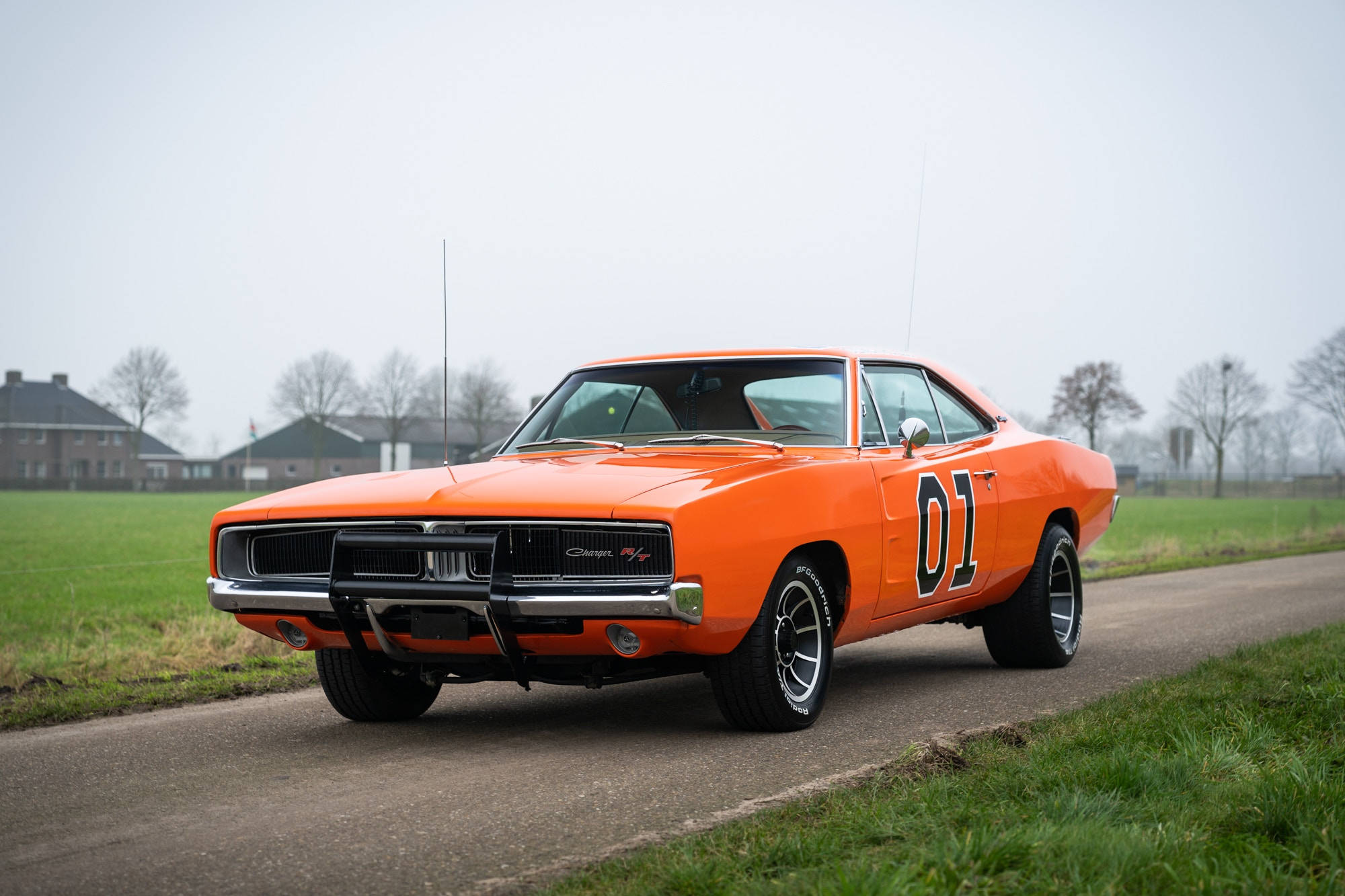 General Lee 桌布 壁紙 — 一輛鮮橙色的1970年道奇Charger R/T，帶有賽車號碼「01」，停泊在鄉村道路上，旁邊是綠色的田野，天空多雲。