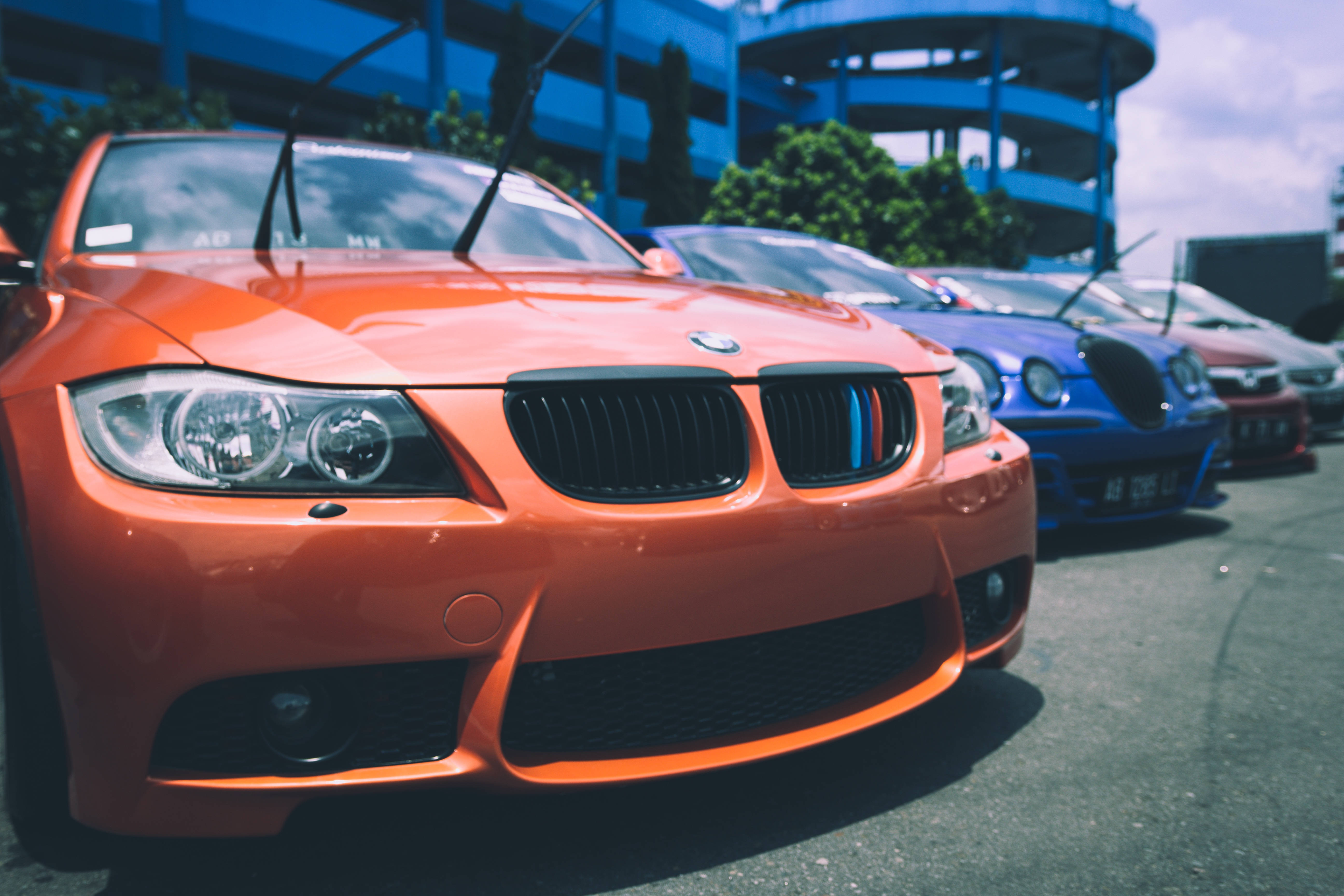 BMW 動圖 桌布 壁紙 — 一輛鮮橙色的BMW跑車停放在停車場，背景有藍色停車結構和其他汽車。
