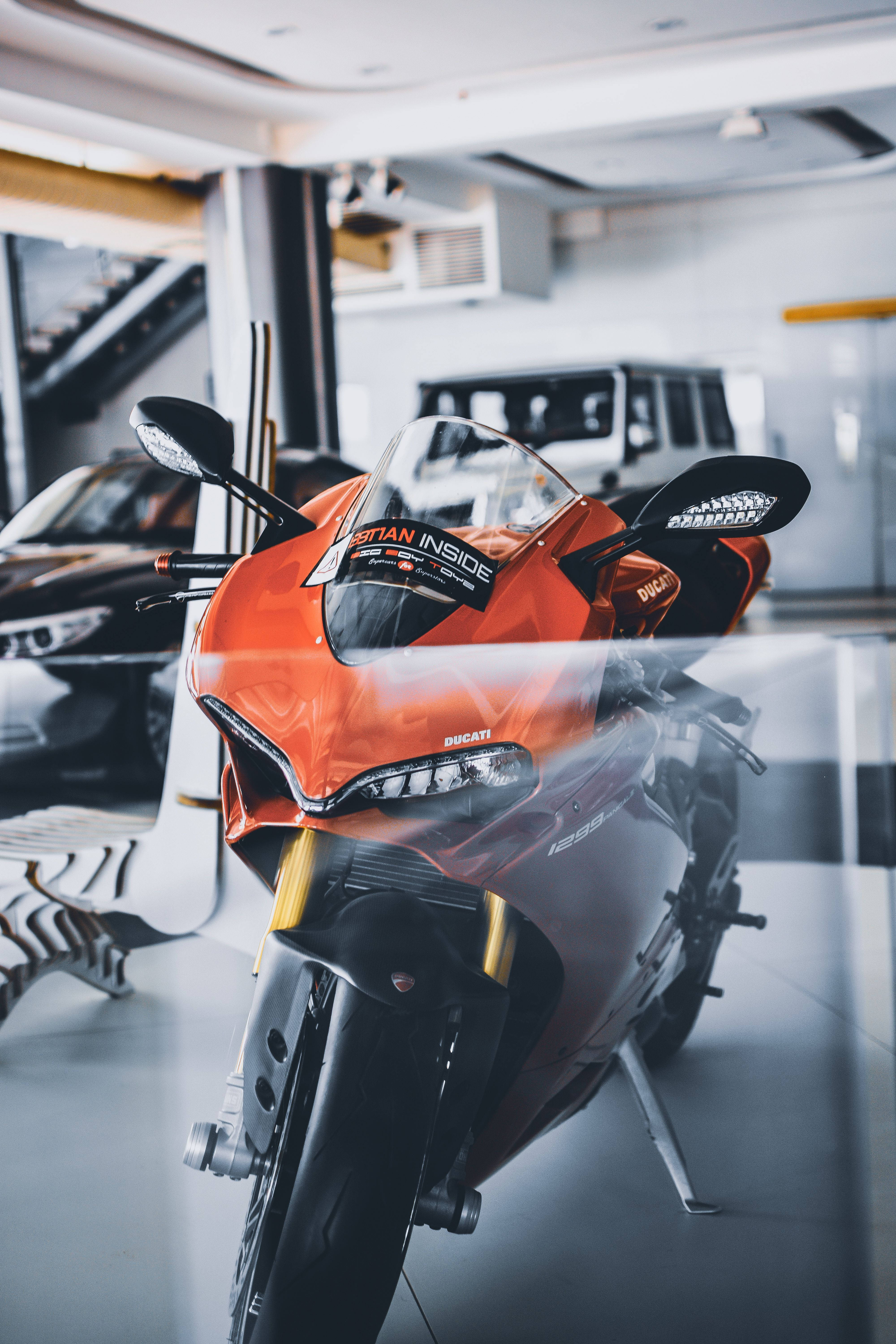 腳踏車 桌布 壁紙 — 一輛鮮橙色的Ducati摩托車在明亮的燈光下，於時尚現代化的展示間中閃閃發光，背景有其他車輛。
