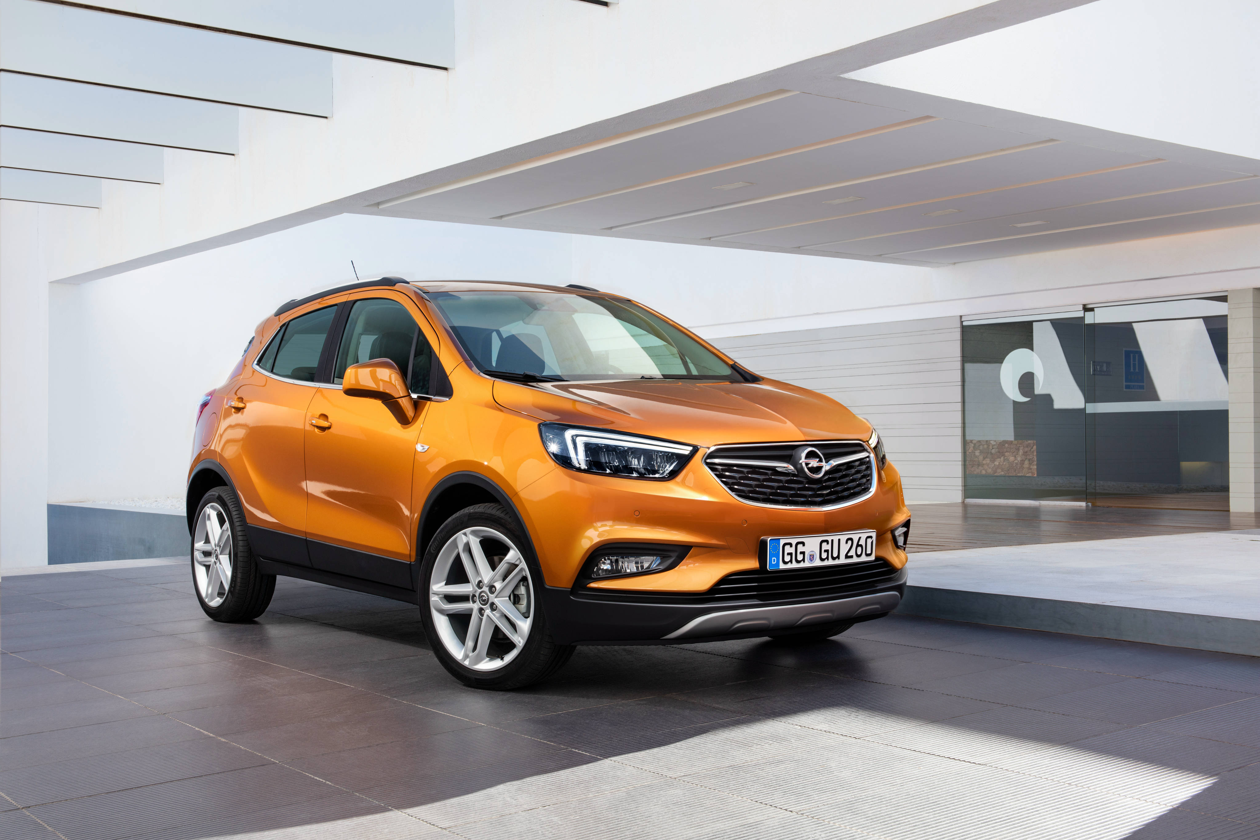 Opel 桌布 壁紙 — 一輛鮮橙色的Opel Mokka SUV停放在現代白色建築結構下，線條流暢，玻璃牆壁。