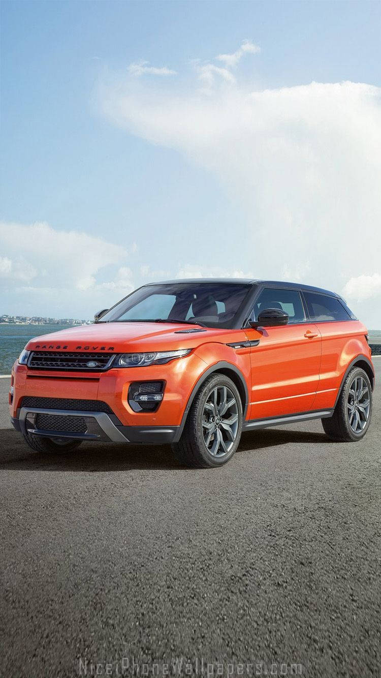 荒原路華 桌布 壁紙 — 一輛鮮橙色的Range Rover Evoque停泊在瀝青路上，天空湛藍，白雲點綴。