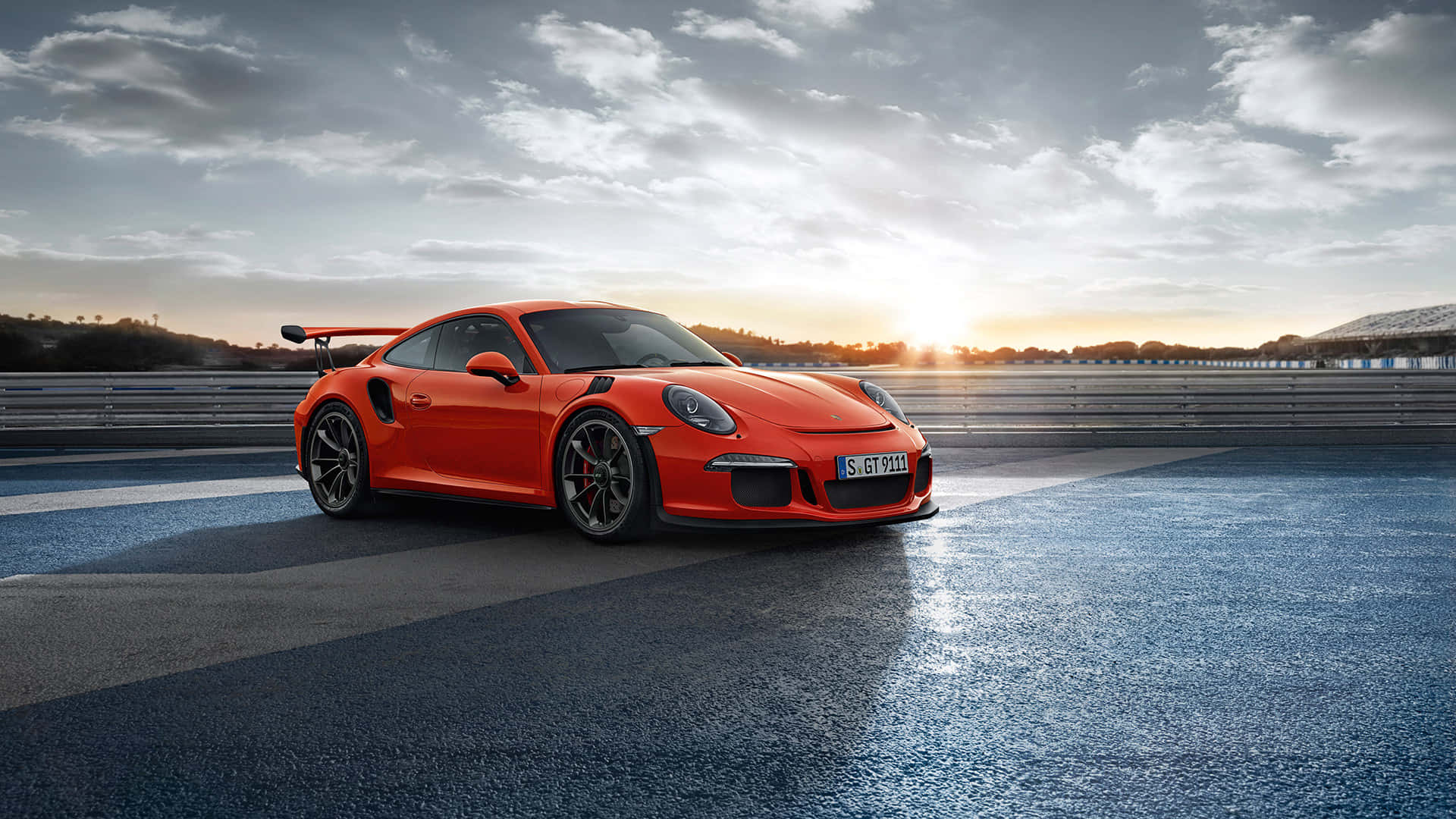 保時捷 桌布 壁紙 — 一輛鮮橙色的保時捷911 GT2 RS停在潮濕的賽車場上，夕陽西下，雲彩壯麗。