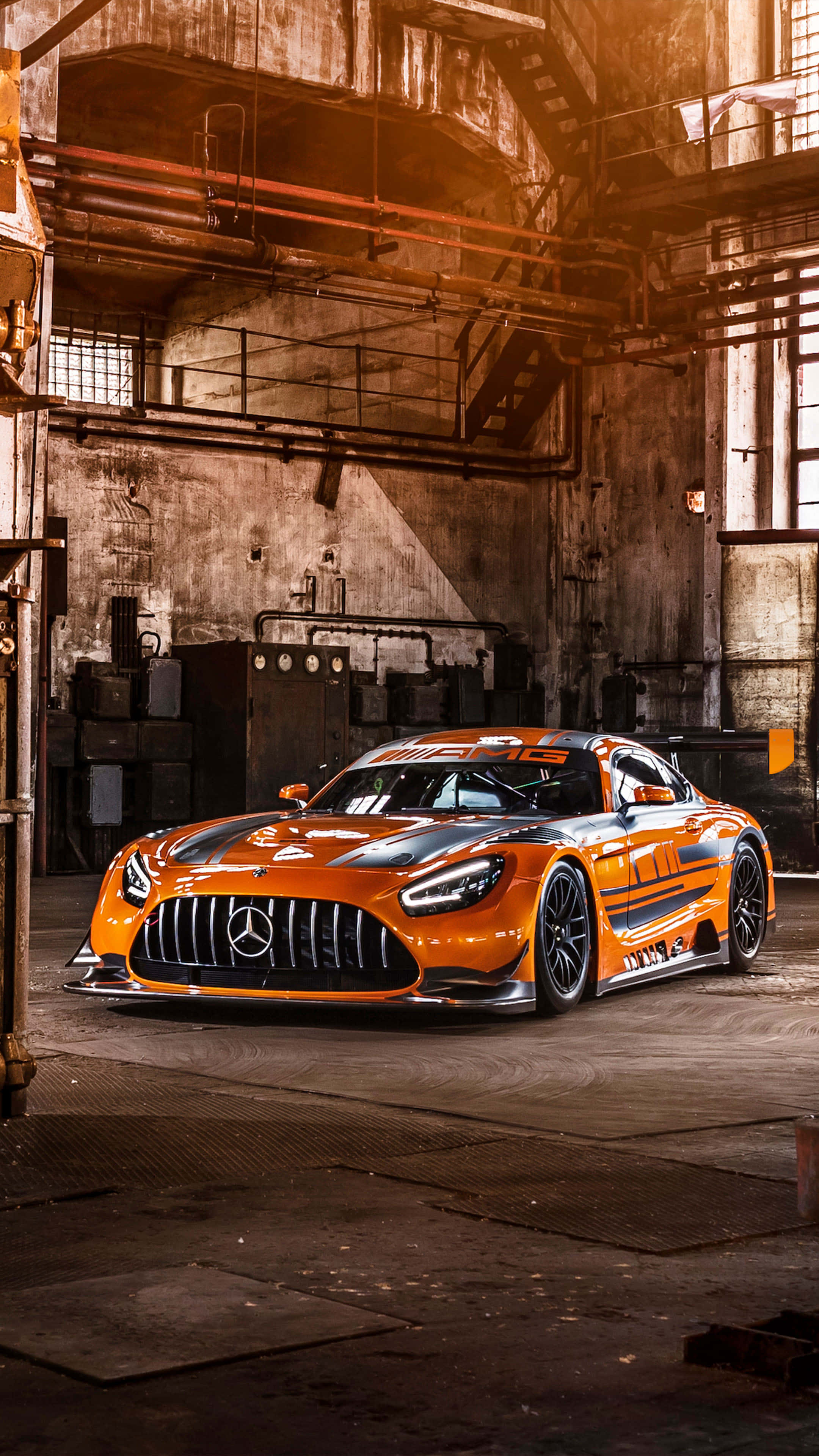 4K 奔馳壁紙 桌布 壁紙 — 一輛鮮橙色的梅賽德斯-AMG GT3賽車在風化倉庫內的溫暖工業照明下閃閃發光。