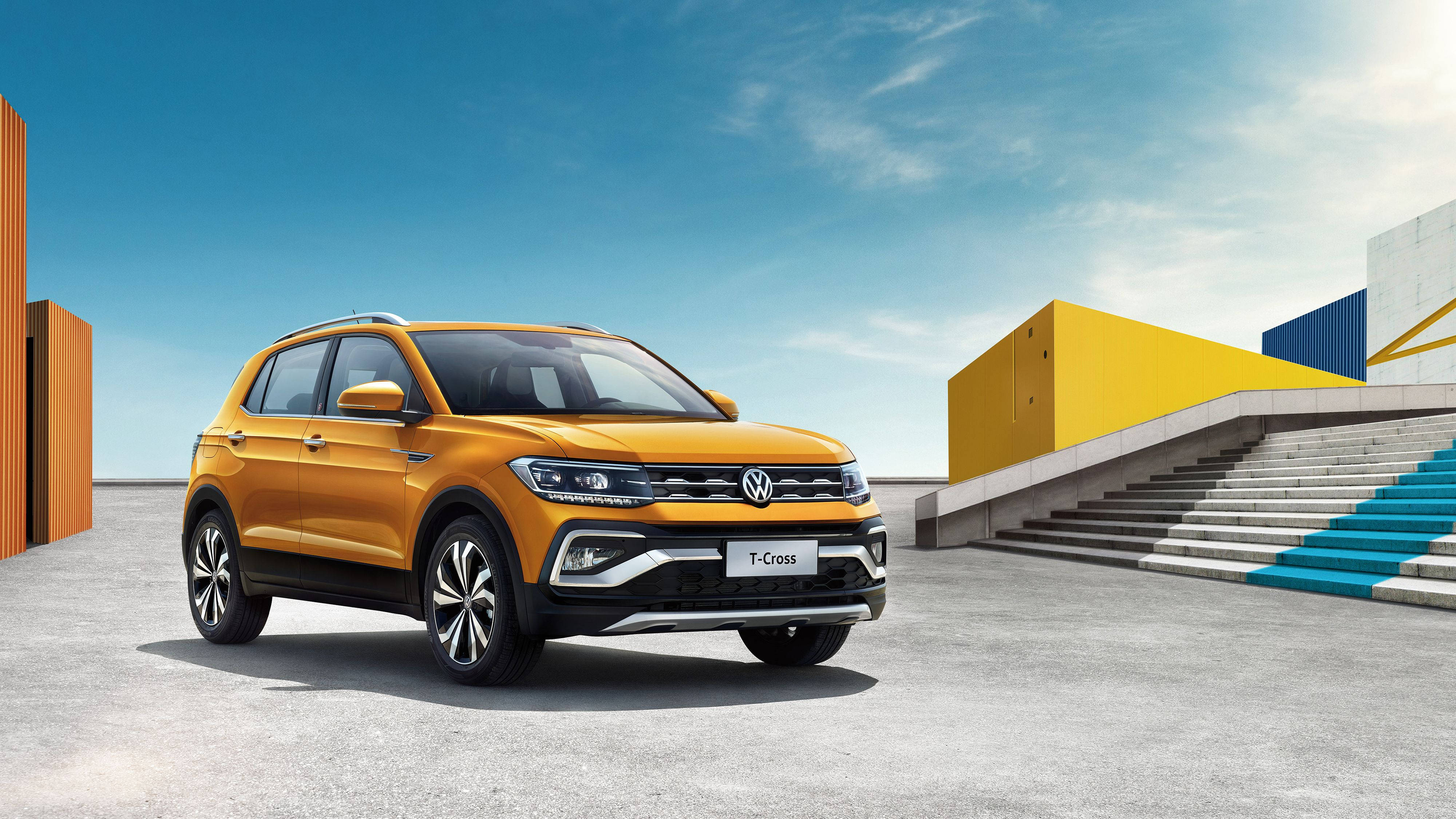 福斯汽車 桌布 壁紙 — 一輛鮮橙色的福斯 T-Cross SUV 停放在混凝土廣場上，旁邊是色彩繽紛的幾何建築，天空清澈湛藍。