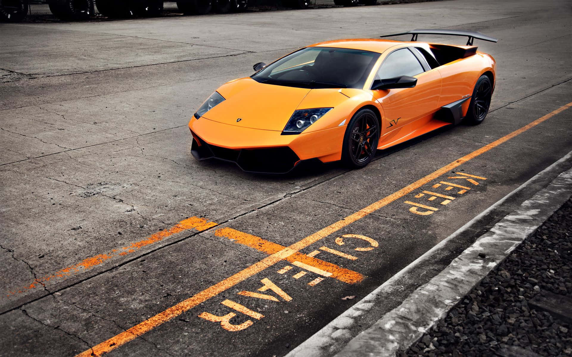 Lamborghini Murciélago 桌布 壁紙 — 一輛鮮橙色的藍寶堅尼 Murciélago 停放在一個佈滿裂縫、帶有褪色 'KEEP CLEAR' 標記的混凝土場地上。